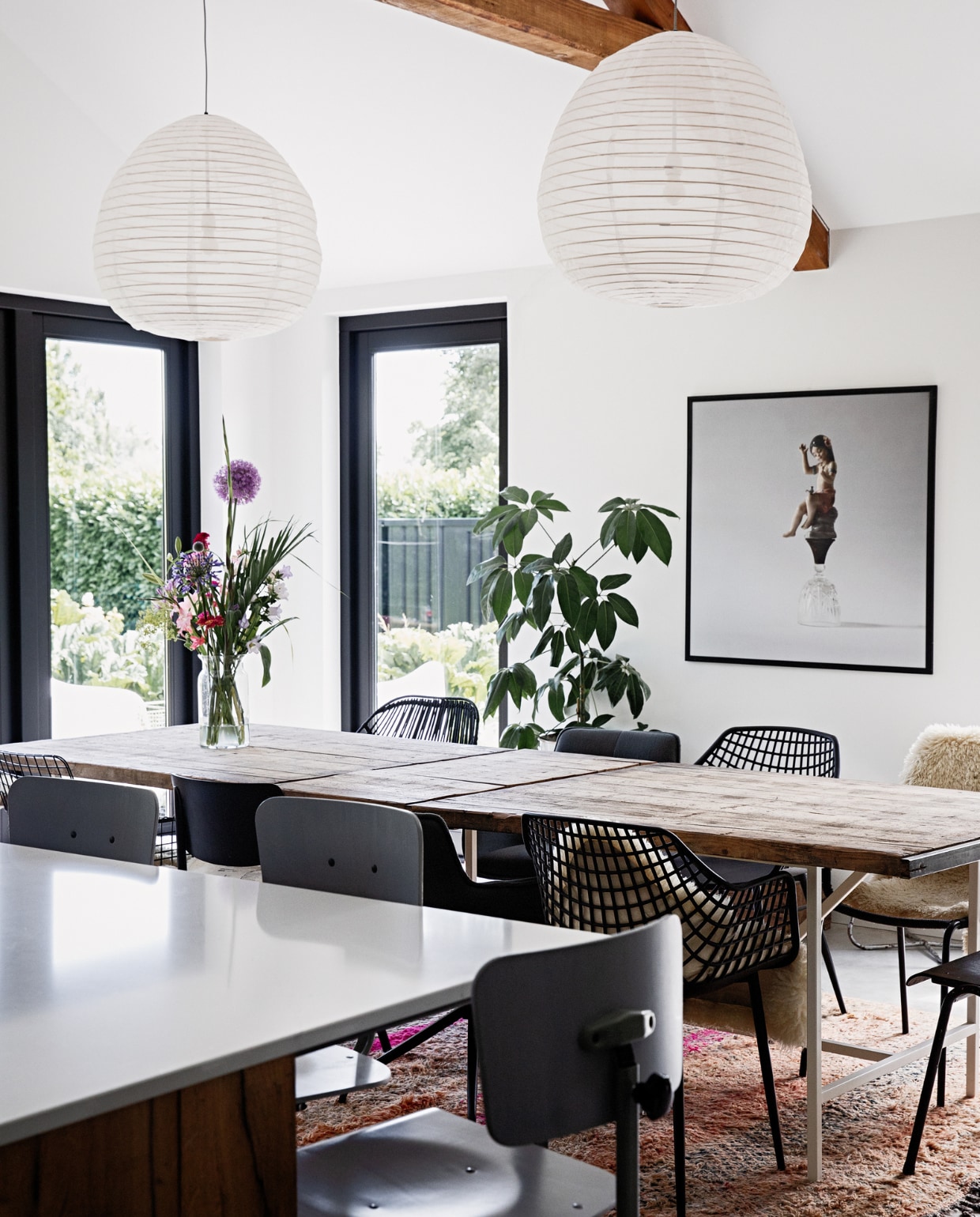 Muurkleur Ral 9016, kleur kozijnen Ral 9005, vloer gevlinderd beton van Bull beton, aanrechtblad De Keukenbladenfabriek, barstoelen De Machinekamer, tafel oude steenschotten op een op maat gemaakte stalen onderstel Gillissen Ontwerp. Stoelen (v.l.n.r. deze kant) draadstoel HKliving, schoolstoel Burbri Antiek, kuipstoel Kwantum, stoffen draaistoel Loods 5, (v.l.n.r. andere kant) zwarte rotan stoel en stoffen draaistoel Loods 5, kuipstoel Kwantum, schoolstoel Burbri met schapenvacht Ikea. Plant gekregen, glazen vaas Bloomon, foto Sake Elzinga, kleed handgemaakt Loods 5. Hanglampen onbekend. vtwonen 12-2022 | styling Ilona Jongepier | fotografie Dana van Leeuwen