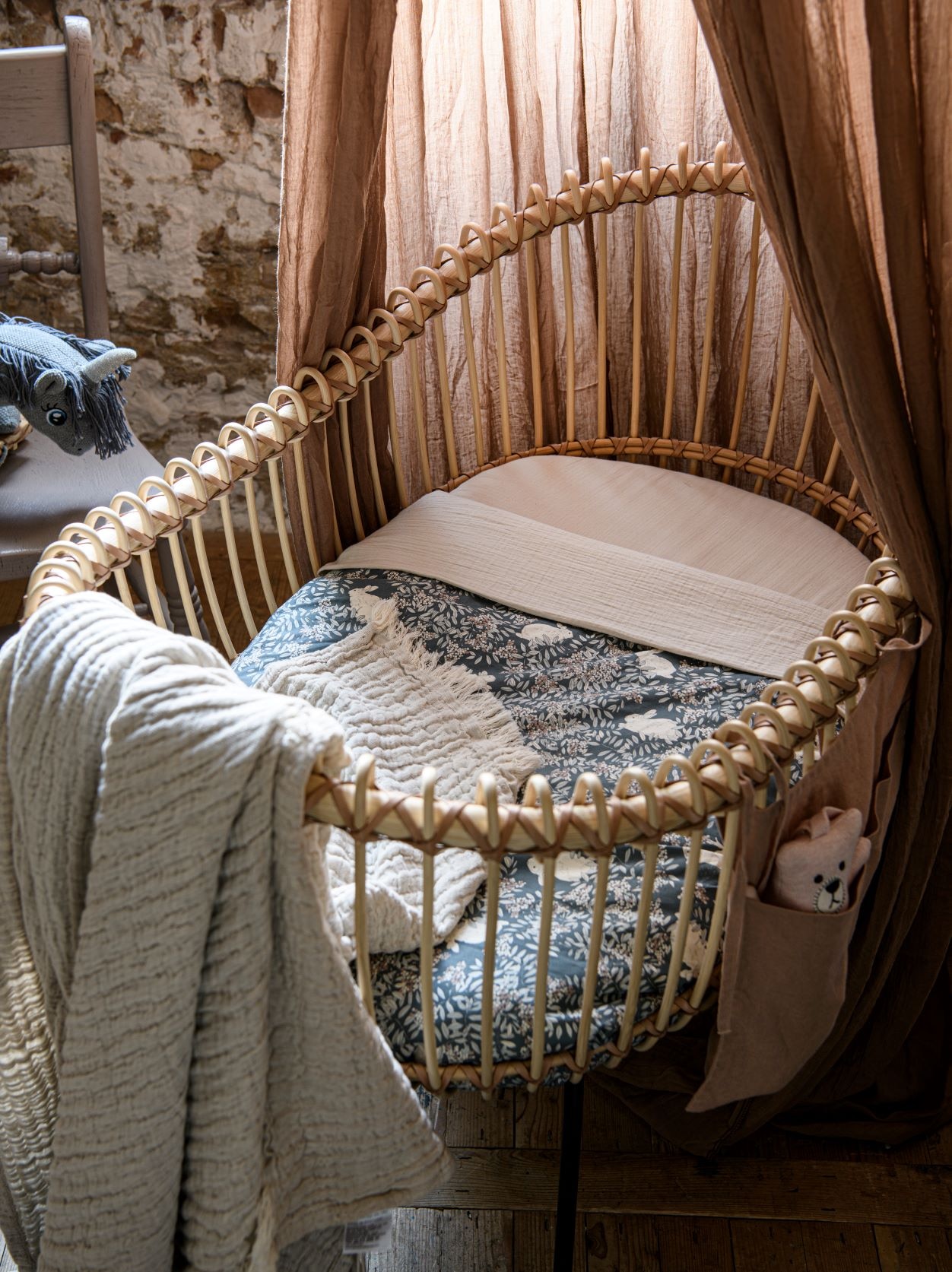 Rotan wieg inclusief matras Loa Crib € 1055,-, linnen insteekzakjes in Cinnamon € 39,-, biologisch katoenen matrashoes van An.nur in Oatmeal, 40×70 cm € 39,-, biologisch katoenen hydrofiele doek € 38,-, blauwe quilt van Garbo&amp;Friends, oeko-tex-gecertificeerd katoen perkal, 90×120 cm € 80,- (thearchivestore.com). Speelgoedknuffel op wielen Unicorn € 74,-, muziekknuffel Teddy Bear € 42,- (coco-mat.nl). Vintage houten stoel, geschilderd in krijtverf Dead Salmon van Farrow &amp; Ball, vanaf € 45,- (com-anders.nl). Katoenen en polyester klamboe Meyco, € 44,95 (bol.com). Plaid Mellow, oeko-tex-gecertificeerd linnen en katoen, 130×170 cm € 90,- (holabb.nl). vtwonen 02-2023 | Styling Marit Saladini, fotografie Louis Lemaire