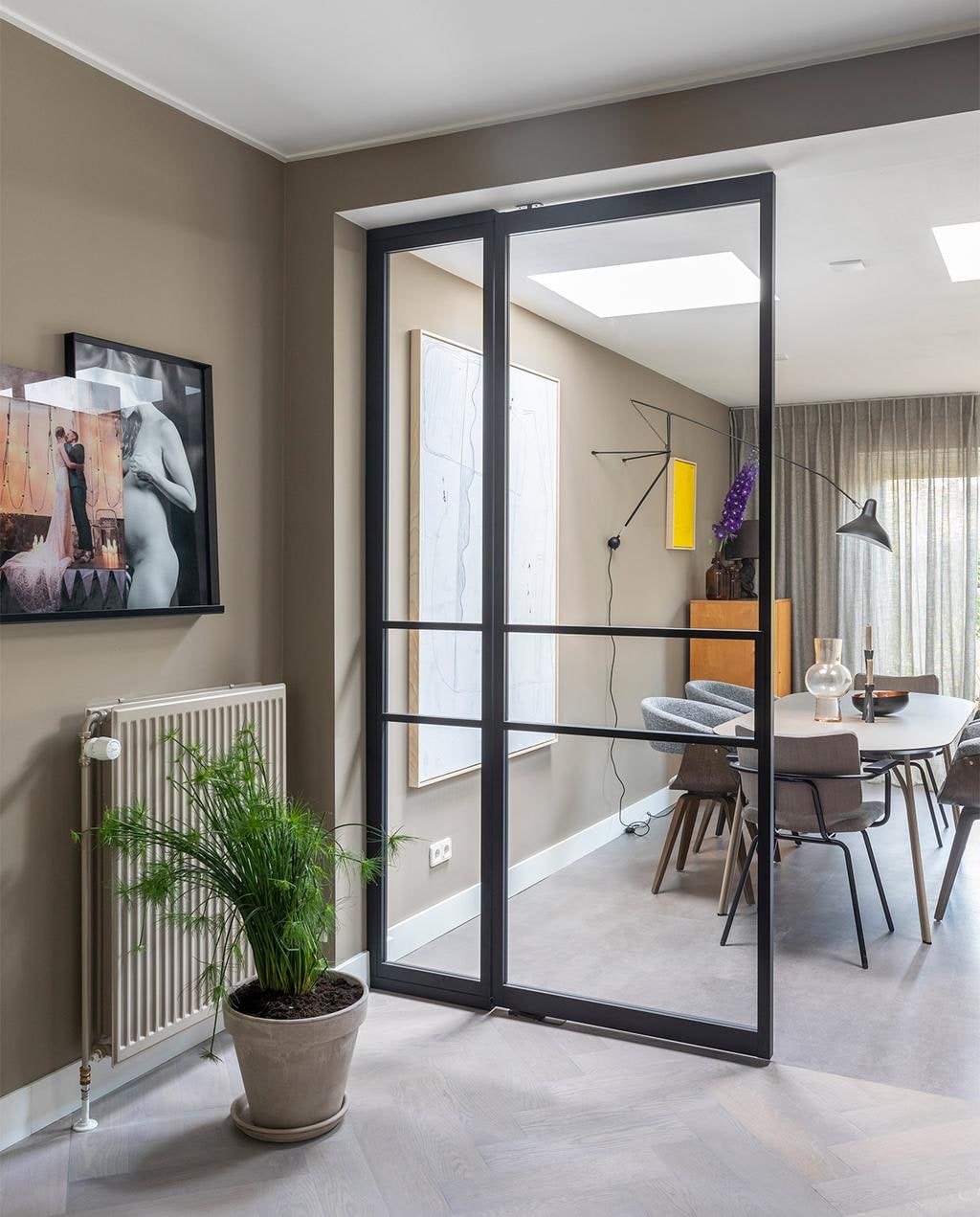 Aluminium tussenwand met deuren prijs op aanvraag (gewoongers.nl). erisde haard € 129,- v€ 309,- € 249,- -,, op maat gemaakt in kleur Chambray Mustard,p per stuk € 13,90,Overig privébezit. 8 t/m 14 Flexa Creations muurverf in de eetkamer Brave Ground, in de keuken Worthy Clay (flexa.nl). Massief eikenhouten visgraatvloer, licht gerookt en afgewerkt met olie prijs op aanvraag, betonlook pvc vloer prijs op aanvraag (woninginrichting- aanhuis.nl). Transparante gordijnen Jetze prijs op aanvraag (eijffinger.com). Aluminium deuren prijs op aanvraag (gewoongers.nl). Oven, kookplaat prijs op aanvraag (atag.nl). Tafel Tree van Woud € 1199,-, grijze stoelen Catch van BePureHome, per stuk € 159,-, bruine stoelen Patch van Bodilson, per stuk € 239,-, zwarte wandlamp Mantis € 950,- (eijerkamp.nl). Groot wit kunstwerk naast tafel Brutalism € 595,-, felgeel kunstwerk € 195,- (hkliving.nl). Hanglamp Marlon € 78,99 (zuiver.com). Tafellamp op de wandplank in de keuken Athens € 73,- (itsaboutromi.nl). Vaas van HKliving € 39,95, zwarte kandelaars per stuk vanaf € 15,25 (vtwonen.nl). Overig privébezit. vtwonen weer verliefd op je huis | seizoen 13, aflevering 8 | styling Fietje Bruijn | fotografie Margriet Hoekstra