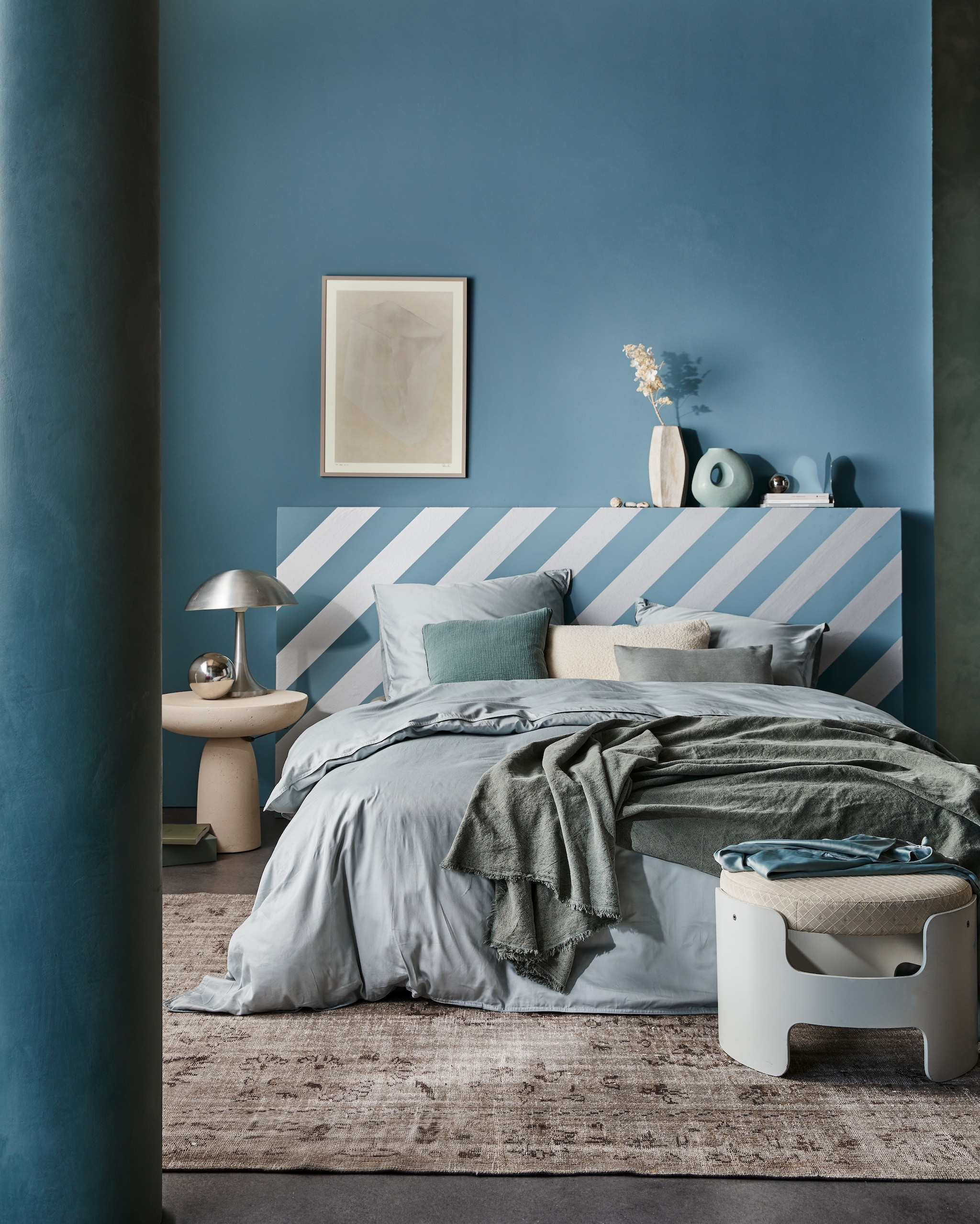 vtwonen collectie behangstrook Silver, 10,66 cm (b), rol van 10 m € 12,99. M.m.v. suite702.nl (satijnen beddengoed in Glacier Grey), neeflouis.nl (poef), edha-interieur.nl (bijzettafel), pietjonker.nl (zilveren lamp), urbannatureculture.com (vazen), rozenkelim.nl (vloerkleed), theposterclub.com (ingelijste poster), zarahome.com (linnen plaid, kussens), vtwonen.nl (muurverf in Old Blue). Overig privébezit. productie Tanja Saarberg | styling Cleo Scheulderman | fotografie Jeroen van der Spek | assistentie Kelly van Gendt | studio en decorbouw Studio Milo