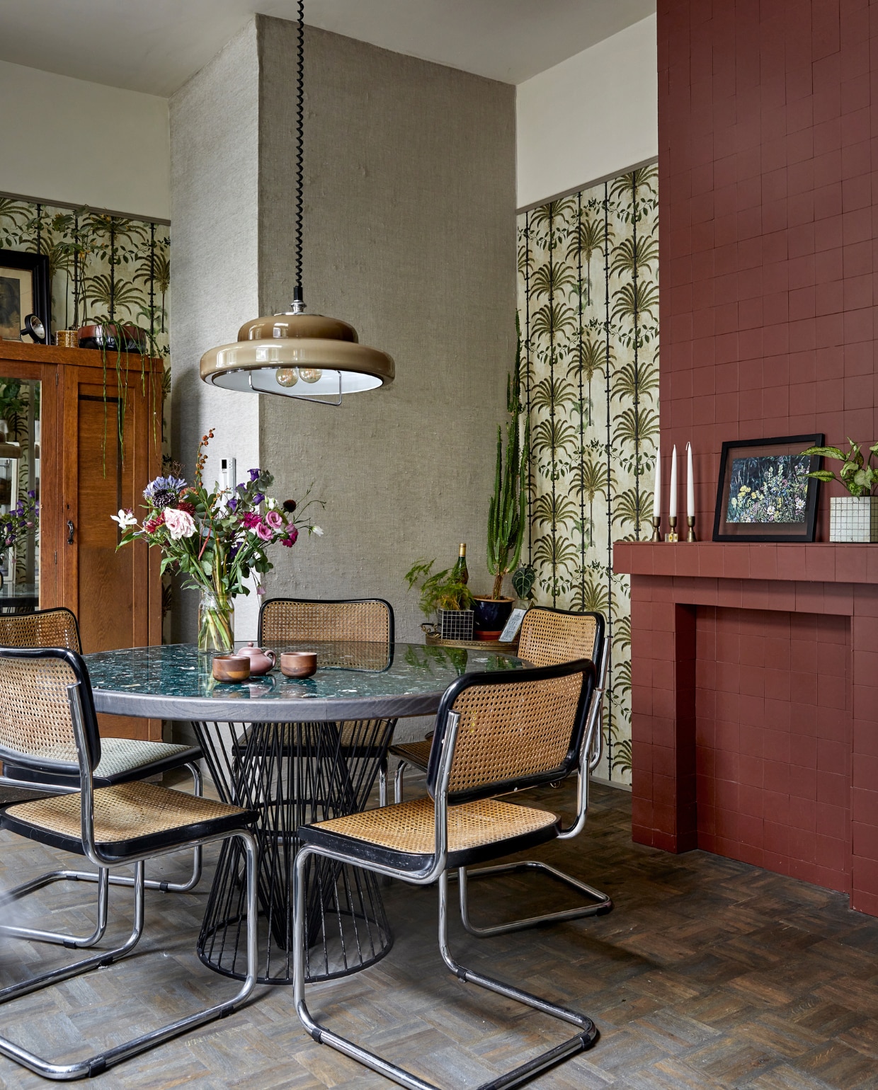 Behang Havana Taupe van Mind the Gap. Tegels haard Winckelmans in kleur Rouge. Tafel met terrazzoblad eigen ontwerp Buroboro. Theepot relatiegeschenk, kopjes Serax. Hanglamp gevonden op straat. Stoelen en kast Marktplaats. Plantenpotten Serax. Ingelijste print op schouw van schilderij gemaakt door Rosans oma. Kandelaars Xenos. Bijzettafel van Bo’s moeder geweest. vtwonen special binnenkijken 2022-3 | fotografie Peggy Janssen
