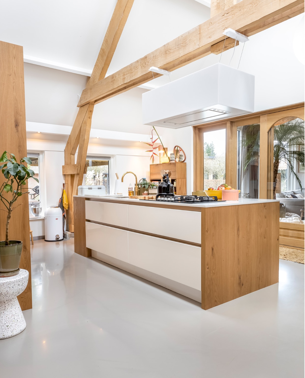 Muurverf en verf plafond RAL 9010, vloer gietvloer. Kruk links HKliving. Keuken Smit Keukens. Pedaalemmer Wesco. Schort Witloft. Kraan Quooker. Fluitketel Le Creuset. Fruitschaal Des Pots. Roze doosje HKliving. Afzuigkap Novy. Kast HKliving. Objecten op kast van links naar rechts: lamp It’s About Romi, spiegel Zara Home, vaas MD Living, bloem Little Shop of Flowers. Overig onbekend. vtwonen 02-2023 | styling Karin van Schie | fotografie Henny van Belkom