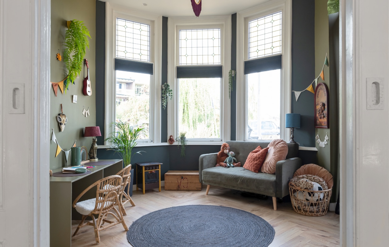 Muurkleur blauw Parcours van Praxis, muurkleur groen Oerwoud van Histor, pvc-vloer lag er al. Bijzettafel, houten fornuis, blauwe tafellamp, plantenpotten en muurbord kringloopwinkel. Kist en bank Marktplaats. Bruine aap en mand Ikea, blauwe knuffel en korte slinger Hema, kussens v.l.n.r. Blokker en MrsBloom. Lange slinger Savanna van Nobodinoz, gitaar New Classic Toys, kunsthangplant Asparagus van Easyplants. Tafellamp Xenos, stoelen Dora via Casa, tegels StoryTiles, giraffe Melissa &amp; Doug, abacus Little Dutch, blik Zeeman, planten Intratuin, vloerkleed Kwantum. Bureau onbekend. vtwonen 02-2023 | styling Sharon Roest | fotografie Caroline Martinot