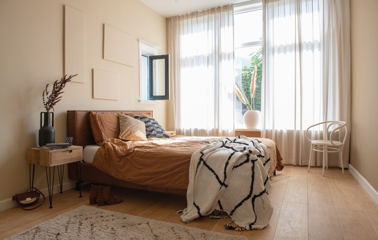 Muurkleur bruin Natural en beige Calm van Praxis. Muurbladeren Kwantum, spiegel Leen Bakker, hanglamp Rope van HKliving. Kast Sklum, tafellamp kringloopwinkel, vaas Shopbywoon, sprei Karwei, beddengoed H&amp;M Home, vloerkleed en bed Wehkamp Home. vtwonen 02-2023 | styling Sharon Roest | fotografie Caroline Martinot