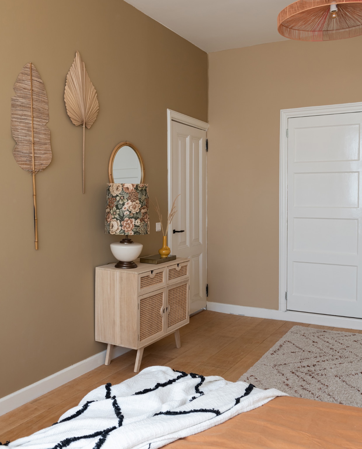 Muurkleur bruin Natural en beige Calm van Praxis. Muurbladeren Kwantum, spiegel Leen Bakker, hanglamp Rope van HKliving. Kast Sklum, tafellamp kringloopwinkel, vaas Shopbywoon, sprei Karwei, beddengoed H&amp;M Home, vloerkleed en bed Wehkamp Home. vtwonen 02-2023 | styling Sharon Roest | fotografie Caroline Martinot