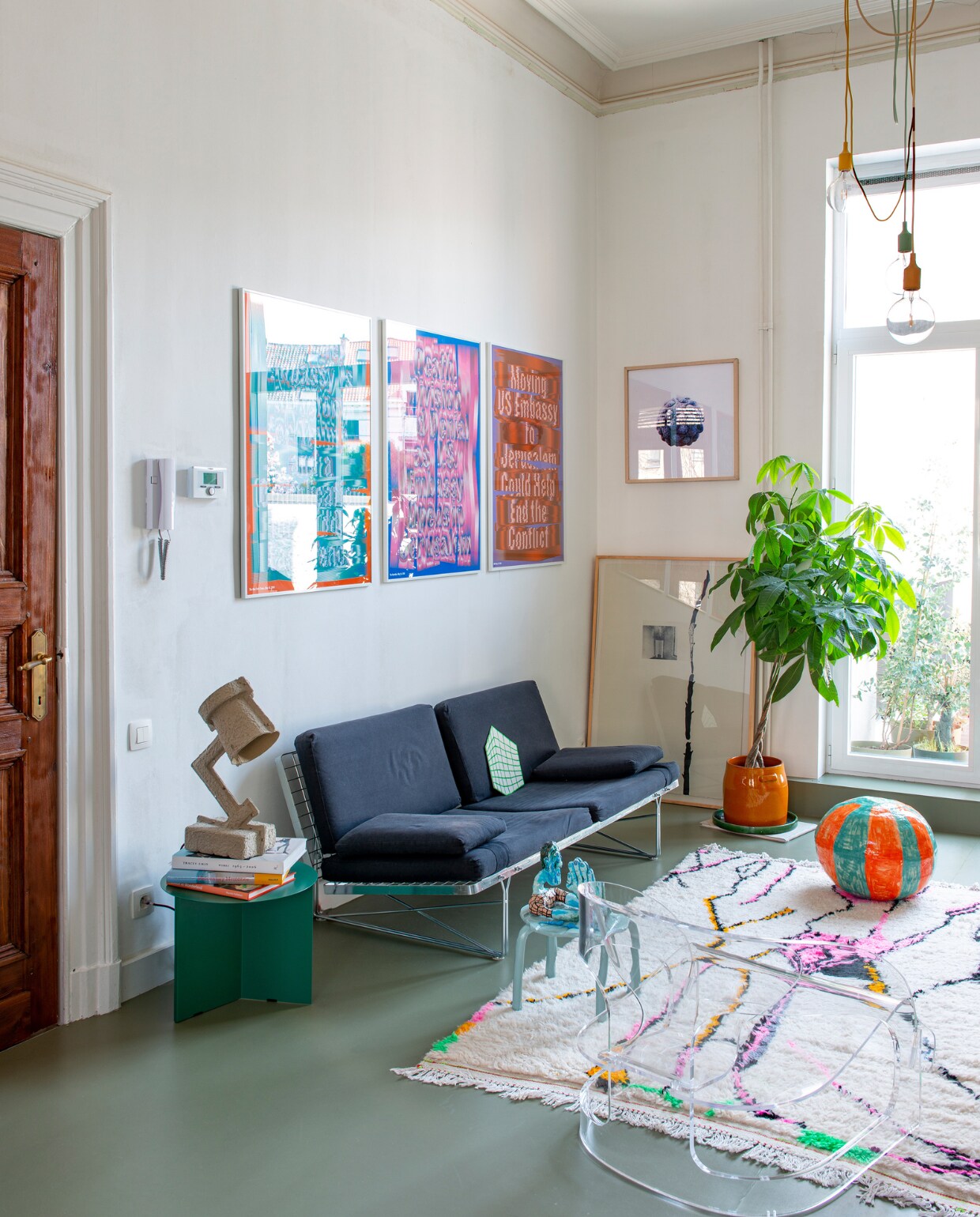 Zeefdrukken Truth’s Triptych van Ward Goes, zeefdruk ernaast Coen Pausma, op de vloer kunstwerk Shelagh Keeley, bank Moment van Niels Gammelgaard voor Ikea, papier-maché lamp Trash Me van &amp;Tradition, groene bijzettafel Slit van Hay, blauwe bijzettafel Sarah &amp; Charles voor Artlead, daarop papier-maché mannetje van Popermacho, transparante fauteuil Joe Colombo voor Kartell, vloerkleed Petit Maroc, bloempot Serax, keramische strandbal Polly Huyghe, hanglampen E27 van Muuto. vtwonen 02-2023 | productie De Binnenkijkers | styling Jeske Weel | fotografie Caroline Coehorst
