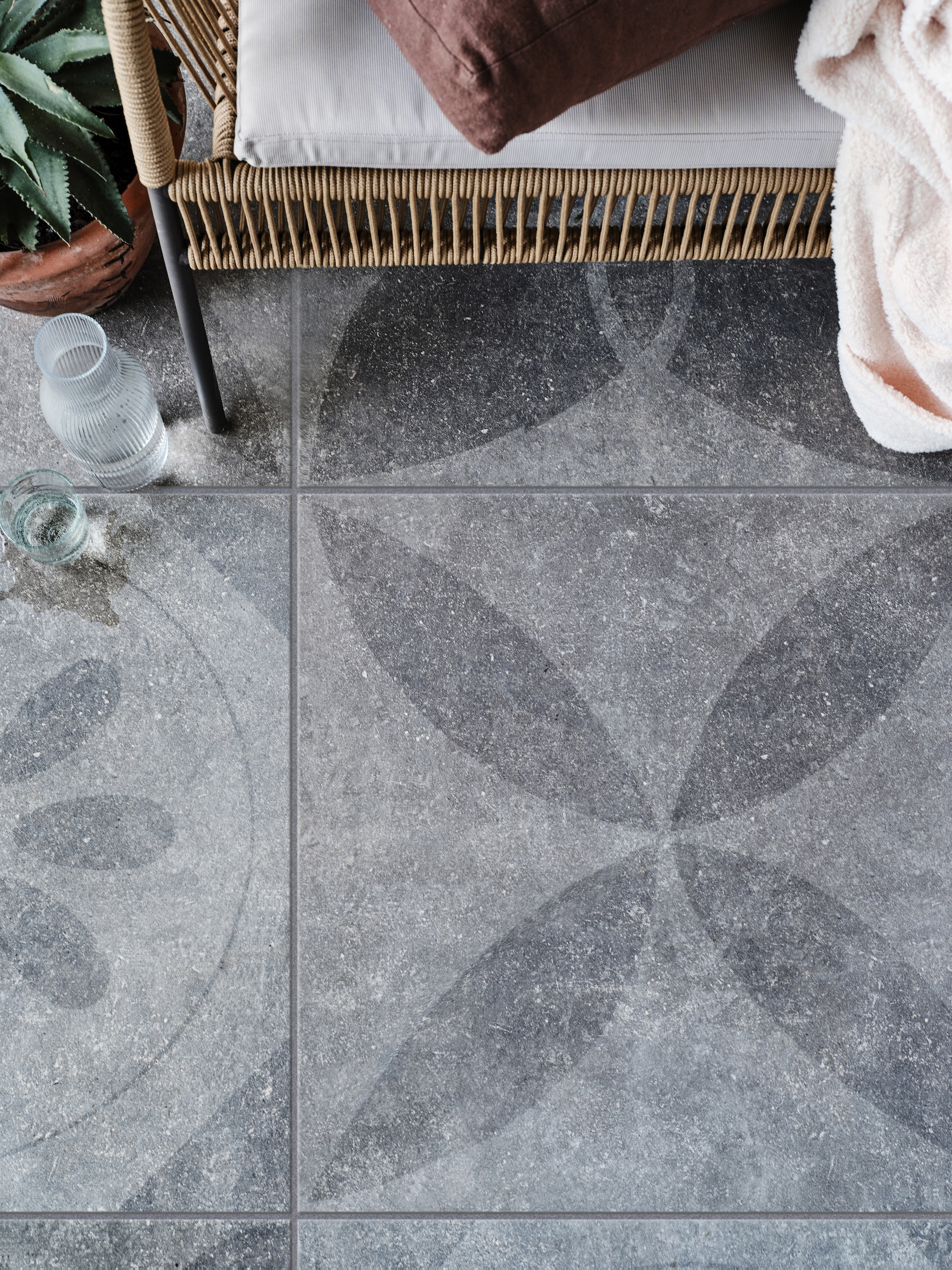 Tuintegel Solostone mix van verschillende dessins: Hormigon Butterfly Antracite, 70x70 cm, per m² € 79,- + Hormigon Floret Antracite, 70x70 cm, per m² € 79,-, Hormigon Flower Antracite, 70x70 cm, per m² € 79,- (ook in 90x90 cm, per m² € 89,50), Hormigon Citrus Antracite, 70x70 cm, per m² € 79,-. M.m.v. vtwonen.nl tweezits tuinbank Samantha van Kave Home, glas en karaf van Serax, householdhardware.nl (tadelakt bloempot, kussen), jolandelijk.nl vtwonen 03-2023 | productie Tanja Saarberg | styling Marlies Does | fotografie Bart Brussee