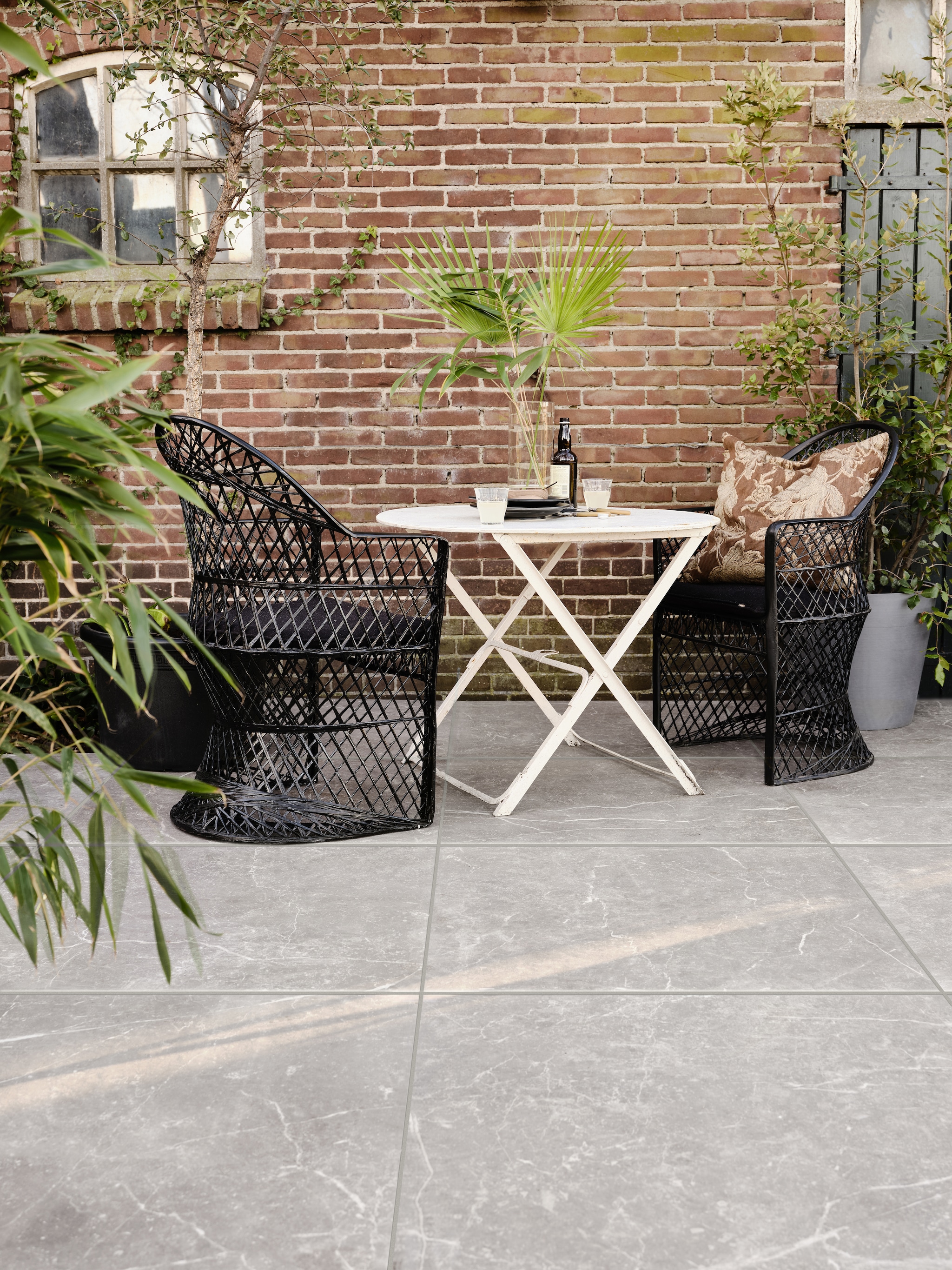 Tuintegel Solostone Outside Marble Warm Grey van vtwonen, 90x90 cm, per m² € 89,50. M.m.v. householdhardware.nl (rotan stoelen, servies), vandijkenko.nl (ijzeren bistrotafel), com-anders.nl (kussen), vtwonen.nl (cilindervaas, grijze pot). vtwonen 03-2023 | productie Tanja Saarberg | styling Marlies Does | fotografie Bart Brussee