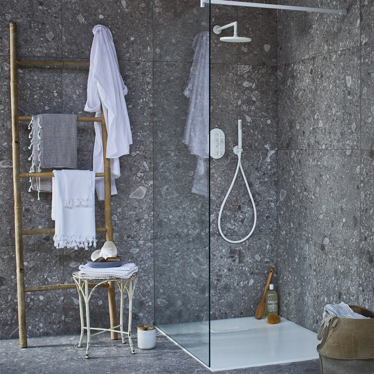 Op de wand en vloer: tegel Composite Dark Grey van vtwonen tegels by Douglas &amp; Jones, douchevloer met geïntegreerde afvoer van gegoten marmer in powder white, glazen douchewand met muurbevestiging in powder white, diverse uitvoeringen (transparant,donkergrijs en spiegelglas), douchekraan Cross, muur-versie powder white met afdekset voor inbouwthermostaat, handdouche, douchearm, hoofddouche. Bamboe ladder, witte badmat op kruk (l’Etoile Conceptstore). Hamamdoeken (Ottomania). Badborstel, nagelborstel (My Deer Store). Witte schaal (Raw Materials). Douchegel, spons (&amp;Klevering). Kruk (Neef Louis). Canvas mand (Hoffz). Schelp (De Weldaad). Pot met kurken deksel (Restored). vtwonen 02-2017 | styling Cleo Scheulderman | fotografie Jeroen van der Spek | productie Inge Steketee
