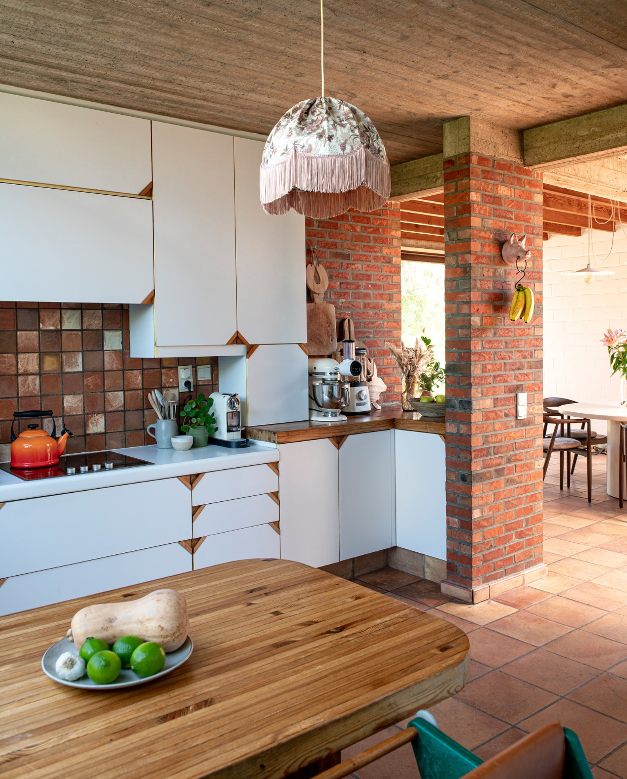 Keuken en tafel zaten al in het huis. Fluitketel Le Creuset. Fruitschaal onbekend. Kinderstoel Hokus Pokus. Hanglamp kringloop. Keukenmachines Magimix en KitchenAid. Potten op het aanrecht kringloop. Varkentje aan de muur souvenir uit Frankrijk. Houten planken tweedehands. vtwonen 03-2023 | productie De Binnenkijkers | styling Jeske Weel | fotografie Caroline Coehorst