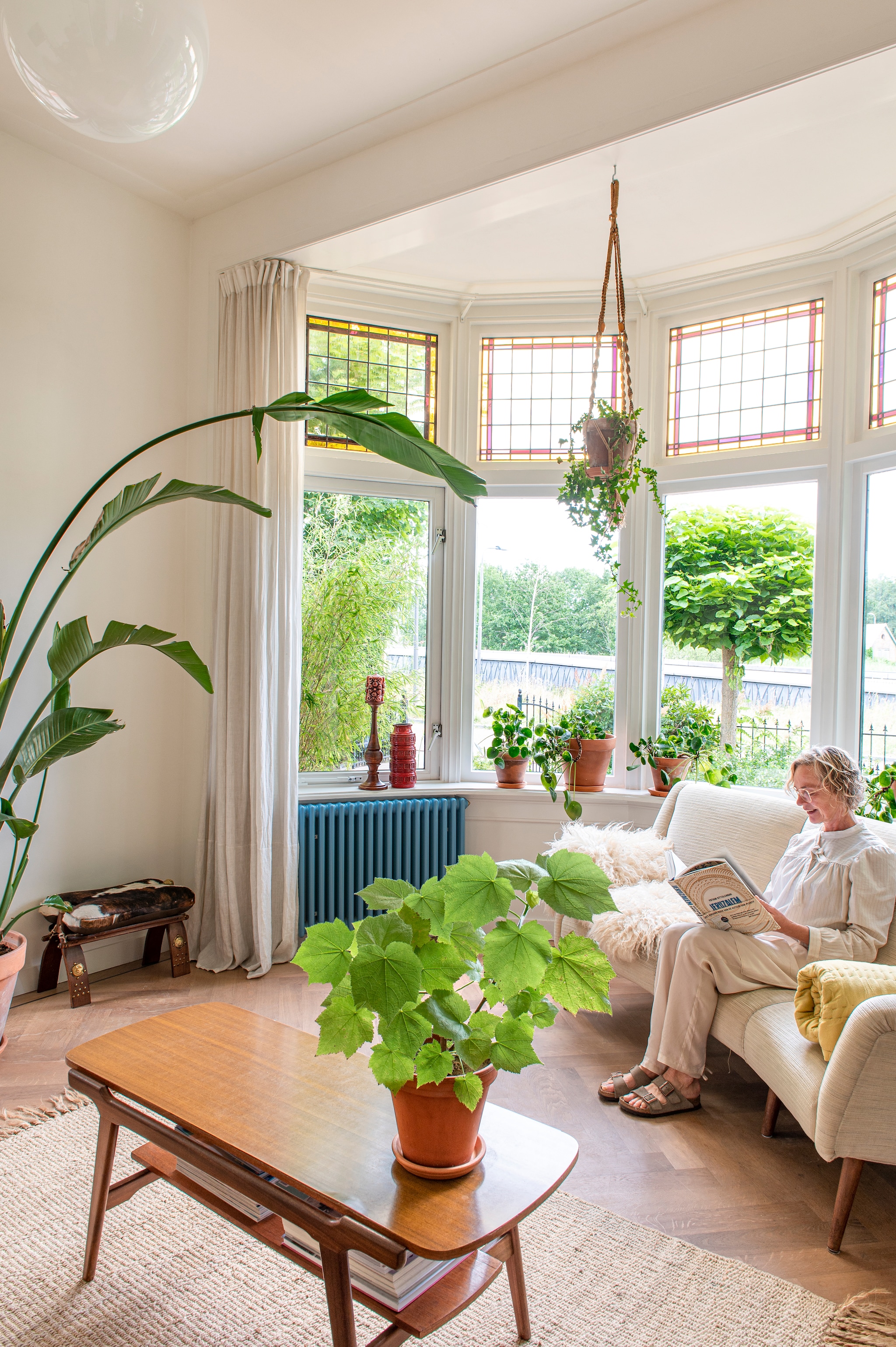 De eikenhouten visgraatvloer lag al in het huis. Verfkleur muur RAL9010. Linnen gordijnen Ikea. Salontafel Louis van Teeffelen. Bank Marktplaats. Gele plaid Loft. Vacht uit Frankrijk. Koeienbank rommelmarkt. Kandelaar en vaas Vanouds. Planten en plantenpotten De Blaakhof. Radiator Zehnder Charleston in kleur RAL5024. Glas in lood verduurzaamd door Van der Staaij ambachtelijke restauratie. vtwonen 03-2023 | styling &amp; fotografie Caroline Coehorst i.s.m. Studio Daan Hietbrink
