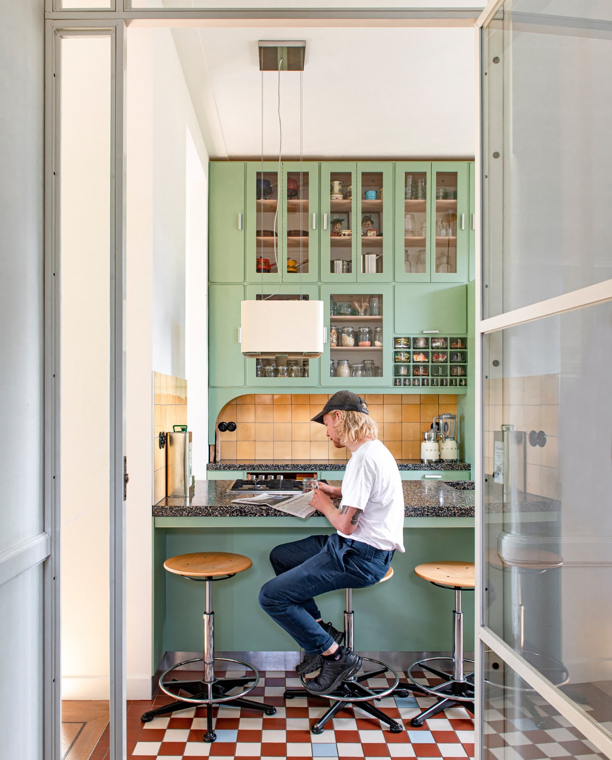 Glazen deuren Goedezaak. Keuken ontworpen door Studi Daan Hietbrink, verkleer fronten Room Green 81 van Farrow &amp; Ball. Keukenblad Marcolina Terrazzo en Beton. Wandtegels en barkrukken Marktplaats. Vloertegels Winckelmans. Blender en melkschuimer Smeg. vtwonen 03-2023 | styling &amp; fotografie Caroline Coehorst i.s.m. Studio Daan Hietbrink