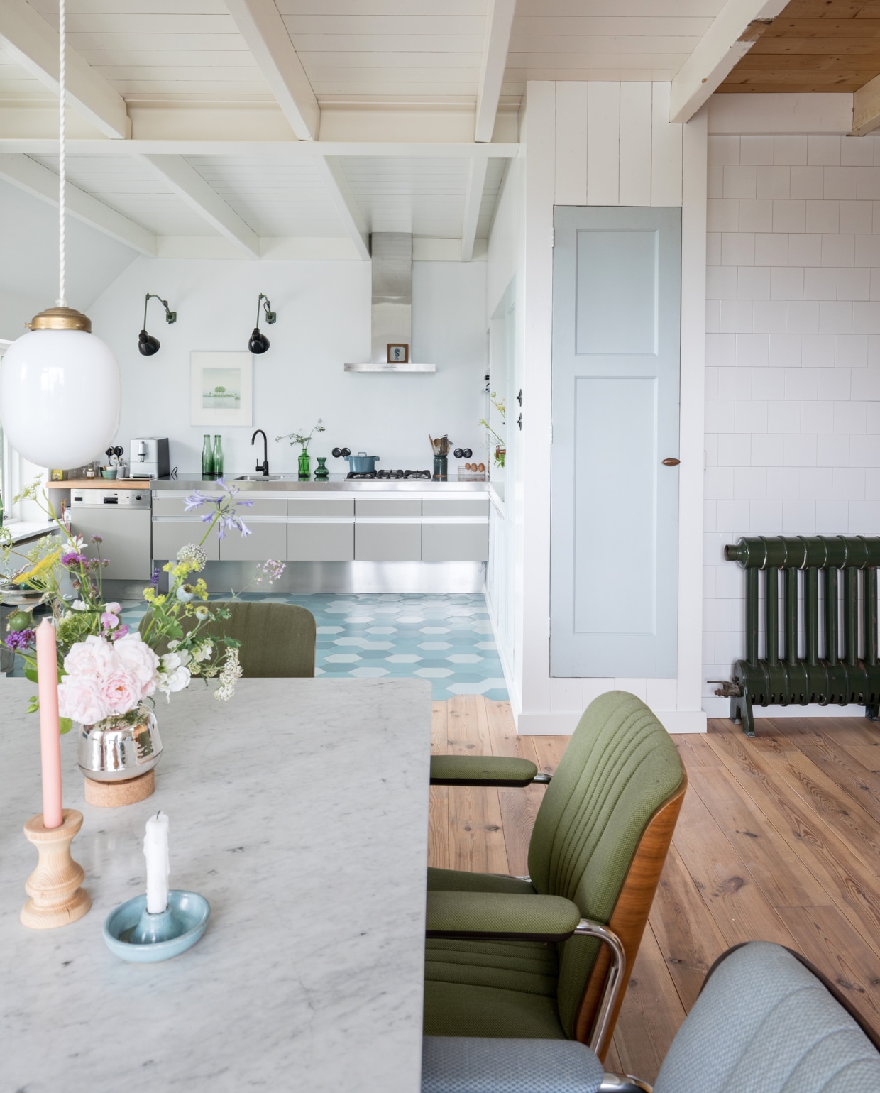 Tafel, vintage Giroflex-stoelen, vintage Siematic-keuken en Kandem-muurlampen Marktplaats. Aardewerken kandelaar rommelmarkt. Hanglamp, houten kandelaar en vaasje uit de winkel van Rixt en Clara, de Sip &amp; Clara Pop-up Store. Antieke radiator van pop-up store in Groningen. Portugese vloertegels Mosaic del Sur. Groen glaswerk rommelmarkt, pan Nicolas Vahé, bakelieten schakelaars Frummes.nl. Kunstwerk Henk Kastelijn, tegel zeepaardje op afzuigkap rommelmarkt. De ijsblauw geschilderde hoge deur is hergebruikt. vtwonen DIY special 01-2020 | styling Sabine Burkunk | fotografie Hans Mossel