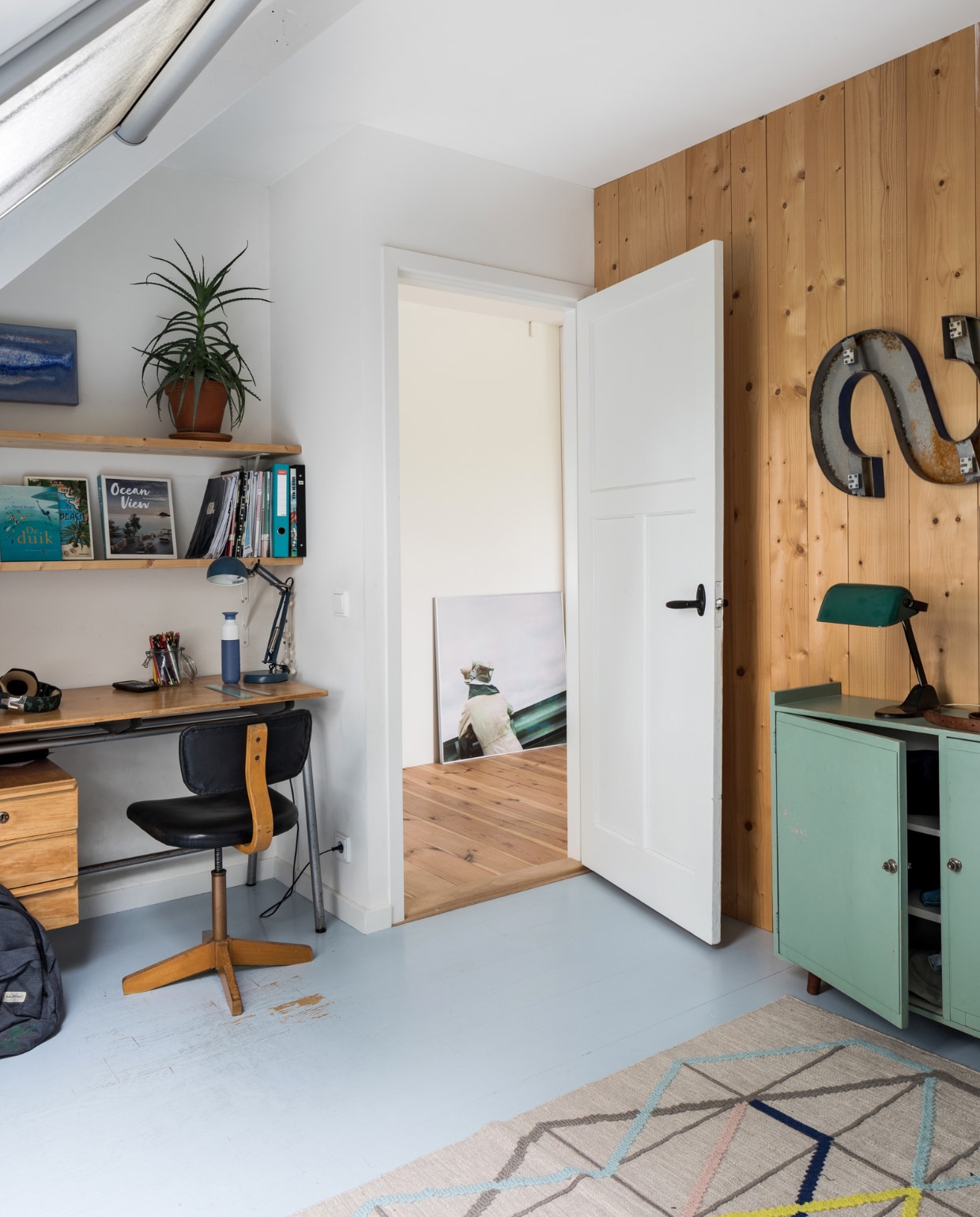De vloer in de kamer van Sef is grijs geverfd. Vintage bureau, bureaustoel, kast en letter S Living Once. Bureaulamp en kleed Ikea. Groene lamp Sip &amp; Clara Pop-up Store. In de gang een antieke foto uit Frankrijk, cadeau gekregen. vtwonen DIY special 01-2020 | styling Sabine Burkunk | fotografie Hans Mossel