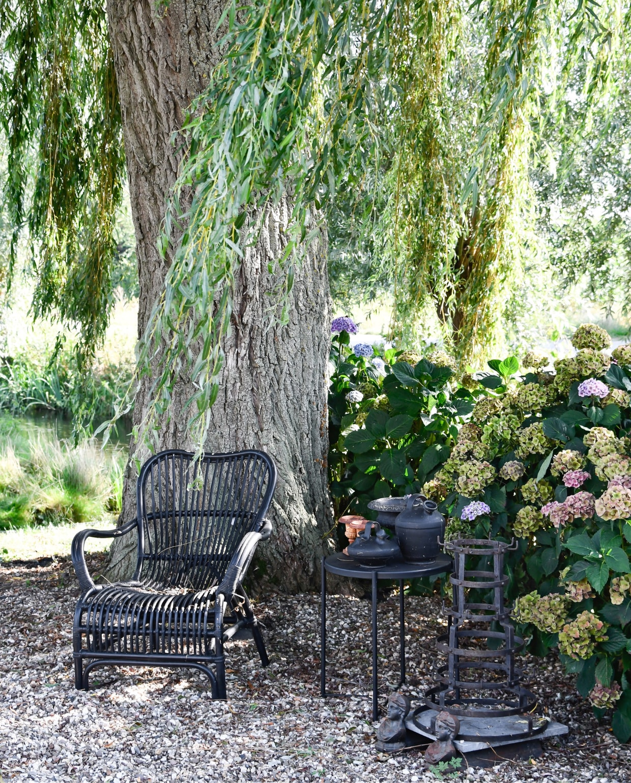 Stoel Jysk, tafel Ikea zelf zwart gespoten, alles erop van de kringloop. Rek rommelmarkt, vrouwtjes onder de steen brocante uit Frankrijk. Onder de treurwilg hortensia’s. vtwonen special tuin 07 | styling Marieke de Geus | fotografie Barbara Groen