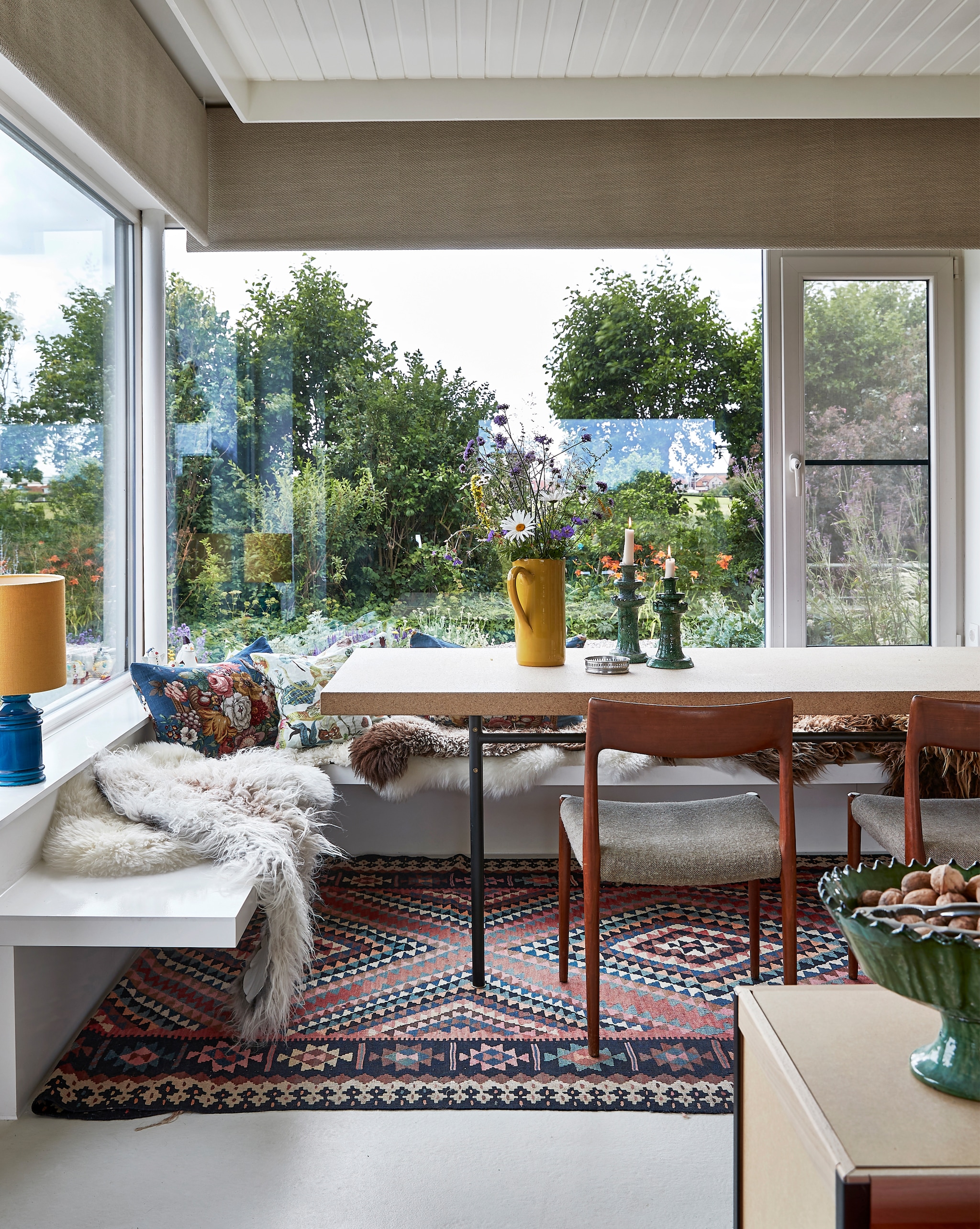 Bank en kussens zelfgemaakt. Schapenvachten her en der gekocht. Tafel Sinnerlig Ikea. Stoelen familiestukken. Schenkkan Villa Augustus. Kandelaars en groene schaal uit Marokko. Vloerkleed uit Istanboel. Tafellamp tweedehands. vtwonen special binnenkijken 12-2022 | productie Living Inside | fotografie Jan Verlinde