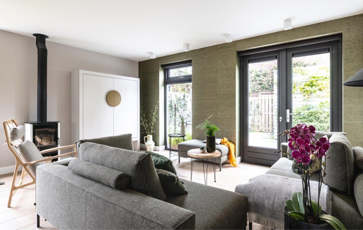 Flexa Creations muurverf kleur Urban Taupe (flexa.nl). Behang Natural Wallcoverings 3 / 303514 prijs op aanvraag (eijffinger.com). Raambekleding Rollerblinds Linbo 08-08-100 L 100 prijs op aanvraag (woninginrichting-aanhuis.nl). DIY: moderne Chinese bruids/tv-kast prijs op aanvraag (remmers-design.nl), geschilderd in Flexa Creations kleur Urban Taupe en handvat in kleur Autumn Gold (flexa.nl). Ingebouwde led-strip prijs op aanvraag (remmers-design.nl). Hoekbank Aikon Lounge van Design on Stock vanaf € 3398,-, fauteuil Dedo van Gazzda € 1540,-, vloerlamp Triangle van HKliving € 269,-, vloerkleed Hem van Ferm Living € 585,- (eijerkamp.nl). Plantentafel € 74,99 (micadecorations.nl). Op zwart tafeltje (privébezit) zwarte kandelaar Hoy Casted van Ferm Living € 79,-, vaas Anse van Ferm Living € 119,-, naast tv-kast handgeschilderde vaas van Return to Sender € 162,95, plaid van Silkeborg Fanø € 119,99 (vtwonen.nl). Overig privébezit. vtwonen weer verliefd op je huis seizoen 15 aflevering 8: Heiloo | Styling Frans Uyterlinde | Fotografie Sonja Velda