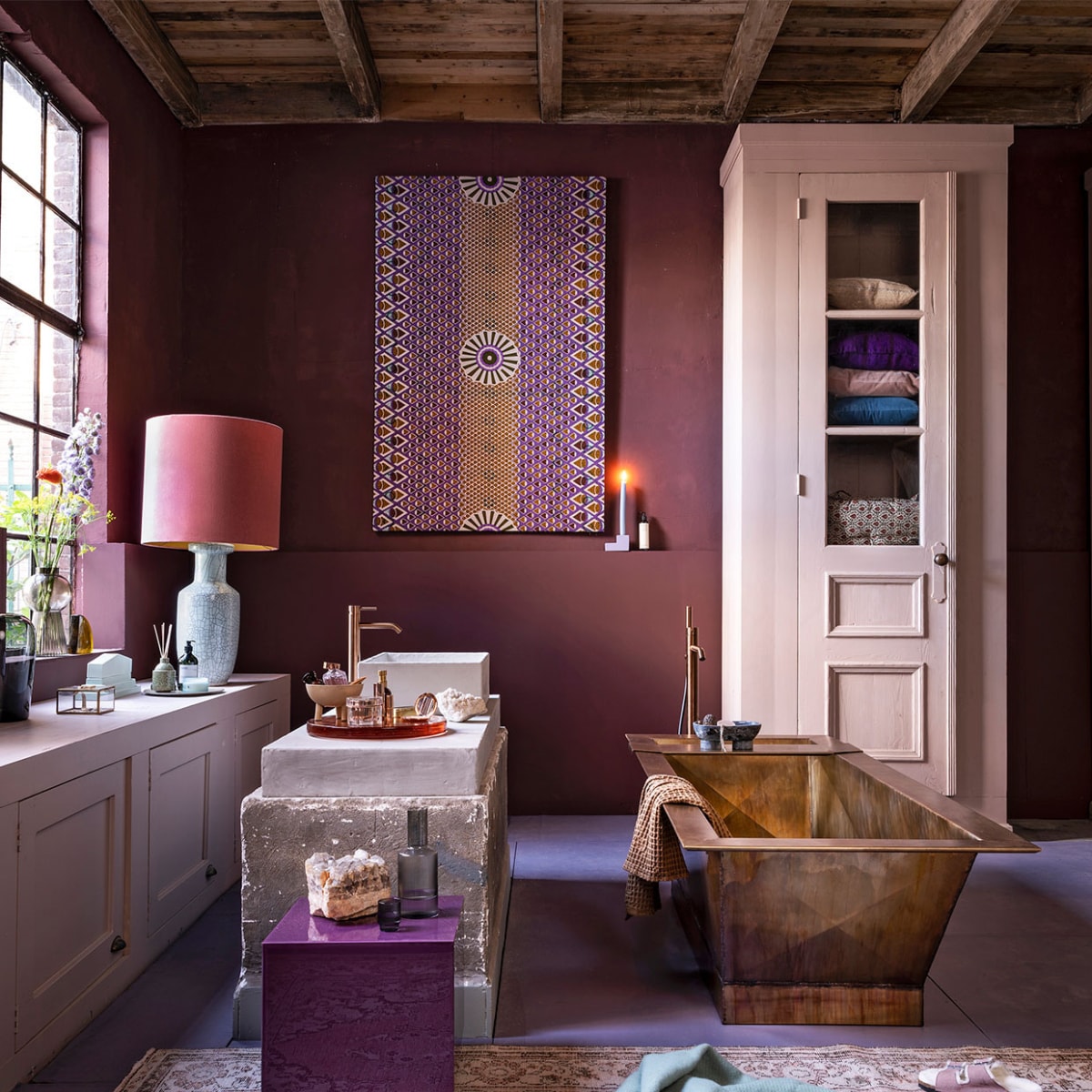 Badkamer aubergine. Op de muur krijtverf Moorland per liter € 39,30, op de vloer lakverf Bohemian per liter € 61,40, verf op de kasten lakverf Old Rose per liter € 61,40 (pure-original.nl). Kasten, beide op maat gemaakt, prijs op aanvraag, wasbak prijs op aanvraag (com-anders.nl). Bad in gepatineerd messing, 2000x815x555 cm (lxbxh), prijs op aanvraag bij de koperslagerij (juliusballer.nl). Losstaande kraan in brons € 2050,-, wastafelkraanin brons € 525,- (jee-o.com). Plexiglazen tafel van HKliving € 195,- (vtwonen.nl). Doek van waxstof item nr. VL40850.365.02 vanaf € 54,95 (vlisco.com). Vloerkleed € 495,- (rozenkelim.nl). Lampenkap € 375,-, lampenvoet € 396,- (polspotten.nl). Glazen vaas van Menu € 69,95, glazen vaas op vensterbank van Bloomingville € 38,99, bord van HKliving € 17,50, waterkan van Ferm Living € 35,-, glazen van Ferm Living per 4 € 35,-, stenen zeepbakje van Ferm Living € 119,-, wafel handdoek van Ferm Living € 39,- (vtwonen.nl). Geel glazen object kwart cirkel van HKliving € 59,95 (deens.nl). Mintgroen keramisch object € 69,95, geurstokjes € 26,95, oranje glazen plateau € 259,- (hkliving.nl). Sieradendoosje € 19,-, kandelaar € 19,95, wollen deken van Hay € 75,- (eijerkamp.nl). Schaaltje op 3 poten € 30,- (101cph.com). Overig privébezit. vtwonen 10-2020 | styling Marianne Luning | fotografie Stan Koolen