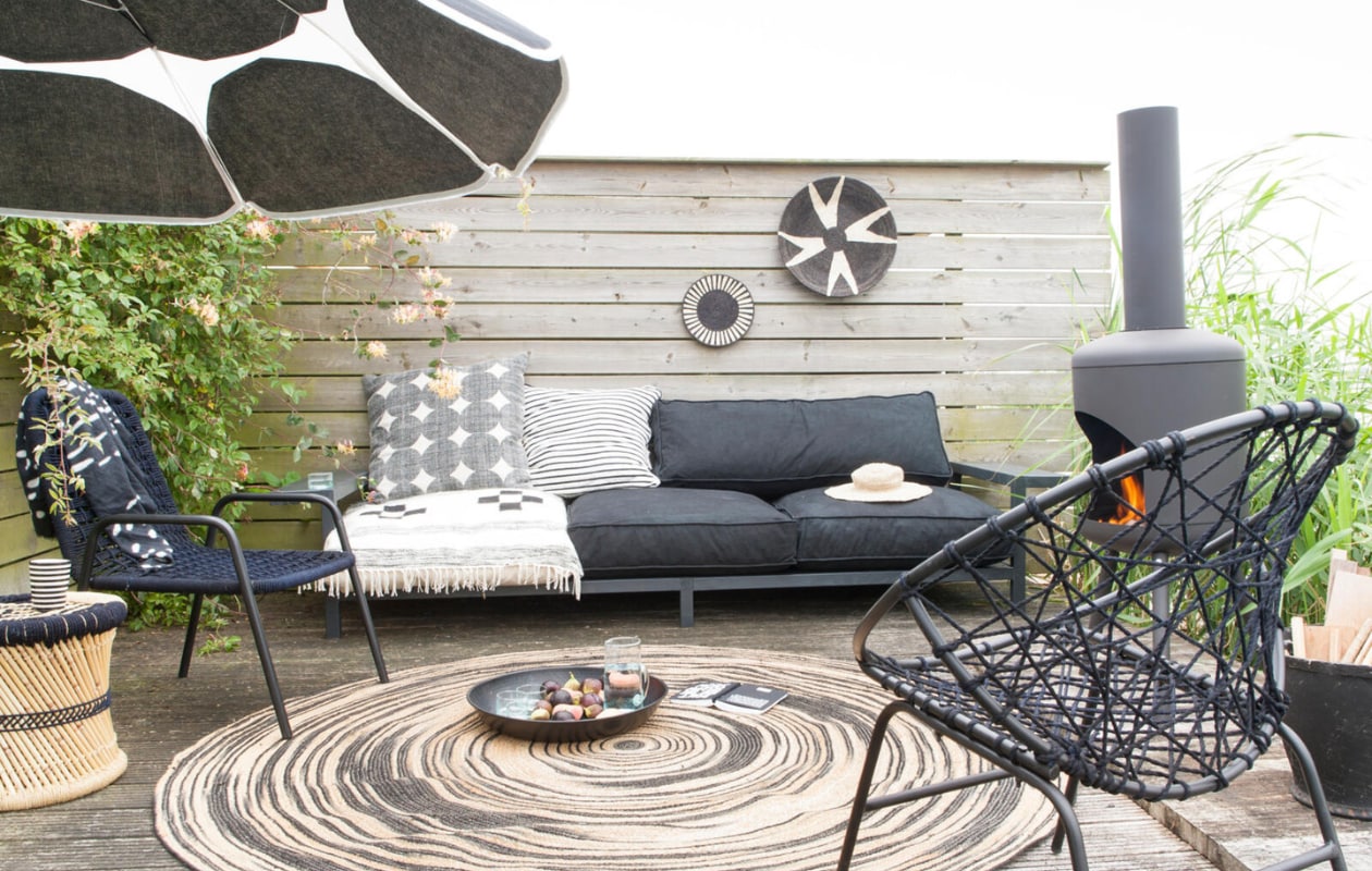 Houten bank met brede armleuningen vanaf € 375,- (Combitex). Zwarte draadstoelen links € 165,- rechts € 299,- (Madam Stoltz). Rond vloerkleed van HK Living, Ø 200 cm € 199,-, terrashaard van RedFire BonFeu € 89,- (www.vtwonen.nl). Rotan kruk van Madam Stoltz, set van 2 € 107,- (www.deens.nl). Outdoor matraskussens, vanaf 80x80x15 cm (bxlxh) € 169,-, rubberen mand € 25,50, gestreepte mok € 9,75, glazen kan € 15,50 (Household Hardware). Kussen met cirkels € 59,- (Sissy-Boy). Jersey kussen met strepen € 69,95 (www.10days.nl). Rechthoekig kussen € 120,- (Trendhopper). Sisal borden vanaf € 29,- (Couleur Locale). Parasolstof met  stippen Kivet per meter € 43,- (Marimekko). Overig privébezit. vtwonen 05-2017 | Styling: Marianne Luning | Fotografie: Anna de Leeuw