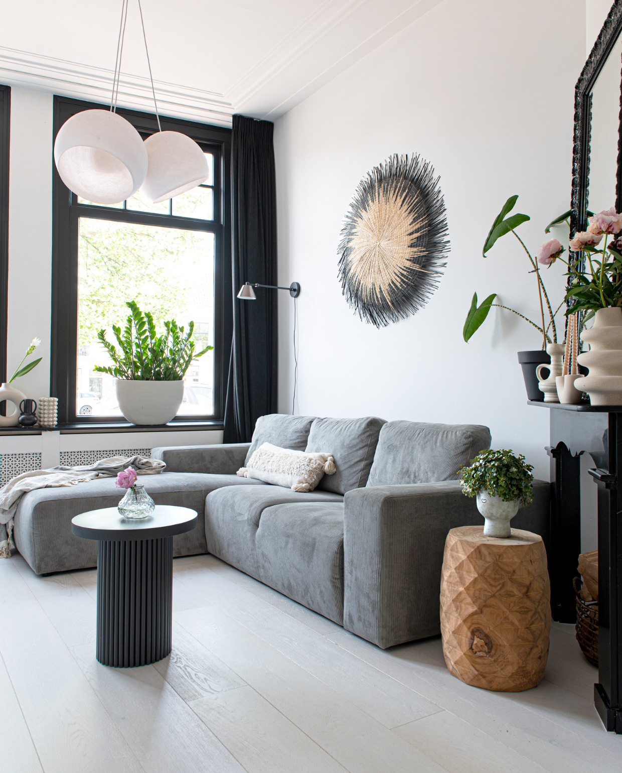 Bank en vaas op zwarte bijzettafel Loods 5, hanglamp Cotton Ball Lights, wandlamp Zuiver, spiegel Marktplaats, kussen H&amp;M Home, handgemaakte wanddecoratie People of the Sun, zwarte bijzettafel eigen ontwerp van Nathalie, houtverf kozijnen Ral 9005. Overig onbekend. vtwonen 04-2023 | productie De Binnenkijkers | styling Jeske Weel | fotografie Caroline Coehorst