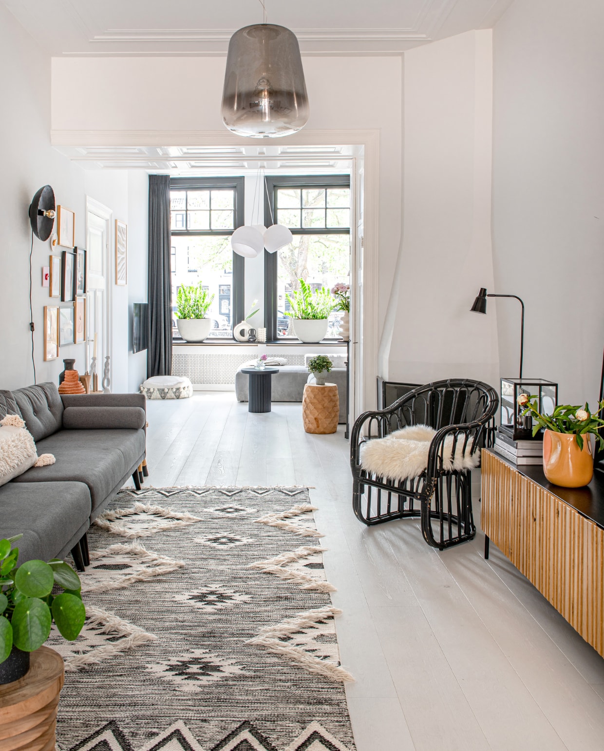 Planten Intratuin, houten kruk Ibiza Outdoor, vloerkleed Rocaflor, bank Sofacompany, dressoir Woood, glazen vitrine en kussen H&amp;M Home, oranje vaas Bloomon, vloerlamp Karwei, fauteuil Ubuntu, wandlamp Casa Gitane, hanglamp Fonq, poef Zara Home. Overig onbekend. vtwonen 04-2023 | productie De Binnenkijkers | styling Jeske Weel | fotografie Caroline Coehorst