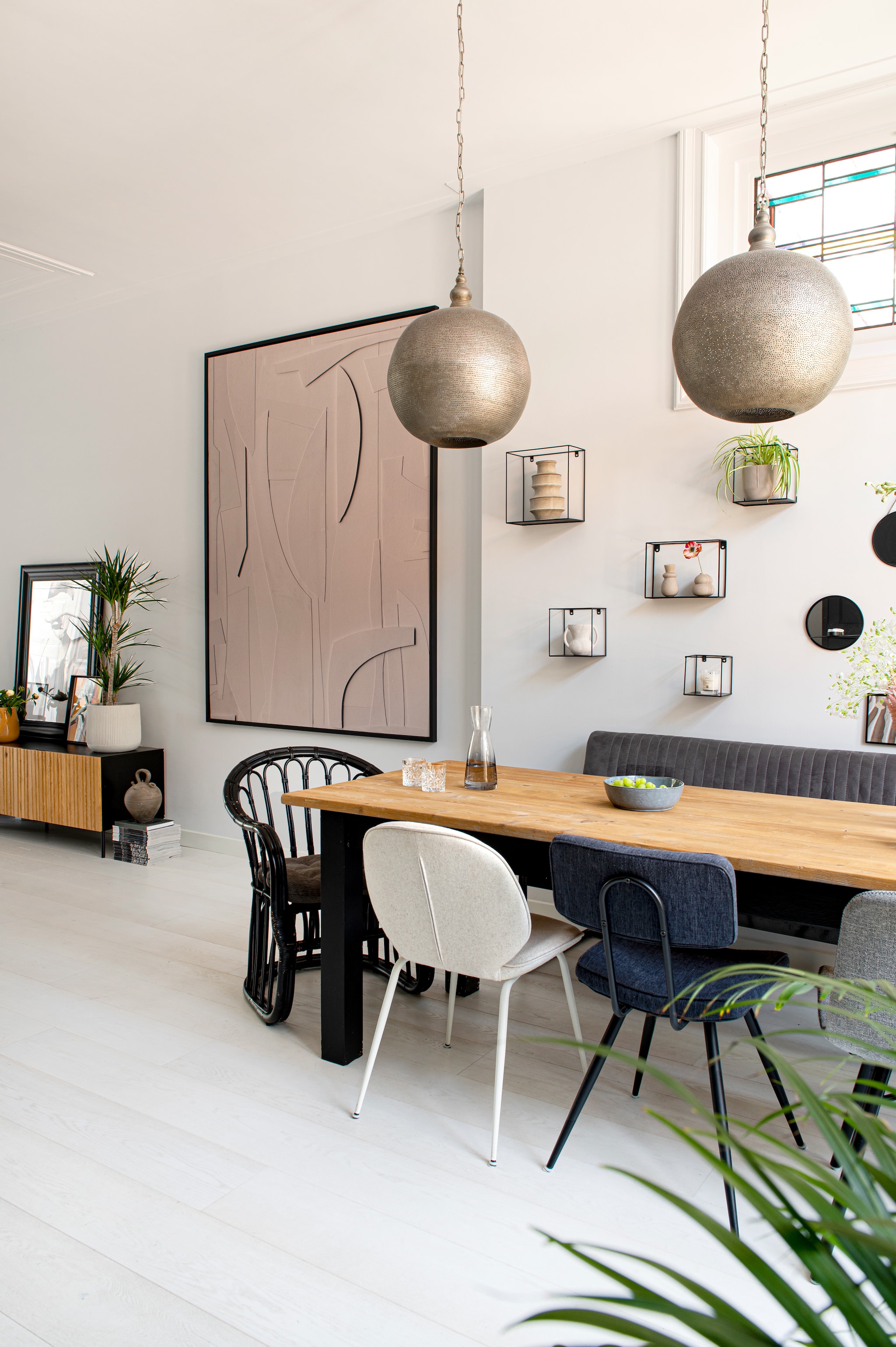 Kunstwerk zelfgemaakt, hanglampen Zenza Home, fauteuil Ubuntu, eetkamerstoelen en  eetbamerbank Loods 5, wandrekken vtwonen, karaf de Bijenkorf, glazen Sissy-Boy, fruitschaal Xenos, dressoir Woood, potten en planten Intratuin. Overig onbekend. vtwonen 04-2023 | productie De Binnenkijkers | styling Jeske Weel | fotografie Caroline Coehorst