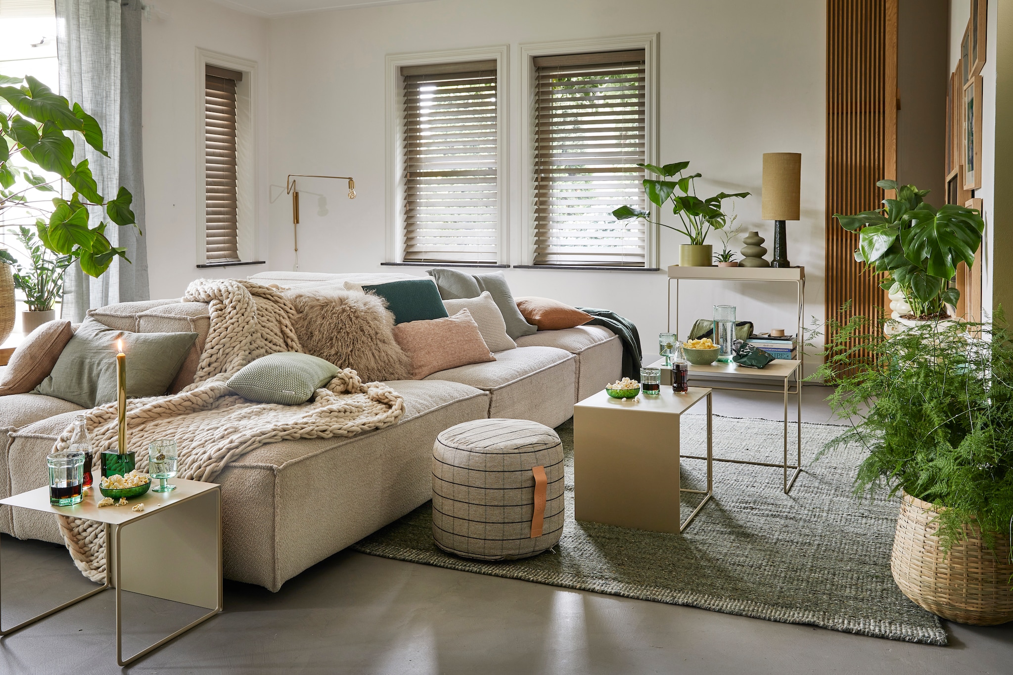 Ecru elementenbank Square van Easy Sofa, per module vanaf € 605,- (hoekbankxxl.nl). Groen geweven vloerkleed Versanti van Linie Design, 240x170 cm € 440,- (vtwonen.nl). Ecru metalen bijzettafel Cluster van Ferm Living, set van 3  € 380,-, grijze geruite poef Grid van Oyoy, 40x38 cm (Øxh) € 104,55, groene kristalglazen kandelaar Parker, 8x3x8 cm € 24,65 (wonenmetlef.nl). Crèmekleurige gebreide plaid, 152x127 cm € 149,- (noirhome.nl). Kussens van links naar rechts: lichtbruin kussen met visgraatmotief Kata van Oyoy, 40x60 cm  € 57,80 (wonenmetlef.nl), linnen kussen Olive, 40x60 cm € 59,- (bymolle.com), kussen Nordic Knit van Marc O’Polo, 30x60 cm € 39,99 (vtwonen.nl), schapenvachtkussen, 40x40 cm  € 69,- (noirhome.nl), groen gebreid kussen  Solid van Malagoon, 50x50 cm € 49,99 (vtwonen.nl), linnen kussen Blush, 35x50 cm € 49,-, gerecycled gebreid denim kussen Sand, 40x60 cm € 79,-, linnen kussen Olive, 60x60 cm € 69,-, linnen kussen Cinnamon, 40x60 cm € 59,- (bymolle.com). Donkergroene merinowollen deken van McNutt, 200x145 cm € 100,-, groen glas van Serax, medium € 9,50, groene glazen popcornschaaltjes Emeralds, 12,5 cm (Ø), per stuk € 12,10, groen aardewerken chipsschaaltje Miscellaneous € 7,- (vanmanenaantafel.nl). Gerecycled wijnglas Oli van Ferm Living € 25,-, gerecyclede glazen karaf Oli Jug van Ferm Living € 39,-, groene kaars Dryp van Ferm Living, per 2 € 11,-, metalen plantenbak op poten Two Tier van Ferm Living, 25x75x80 cm € 299,-, fotolijsten aan rechter wand, vanaf € 35,- (byjensen.nl). Plant Philodendron, groot € 149,95, bamboe mand € 200,-, op side table plant Philodendron € 22,50, groene metalen pot € 35,-, plant rechts Monstera € 28,95, plant voor Asparagus € 44,95, bamboe mand € 89,- (stadstuindebloemenpoort.nl). Messing wandlamp Swing van House Doctor, 65x35 cm € 199,-, mosgroene keramieken vaas Eminent Circles, medium € 49,99, keramieken tafellamp Stoneware met lampenkap van HKliving € 209,- (vtwonen.nl). Terracotta bloempot Rosa, 12 cm (Ø ) € 9,50 (bymolle.com). Lichtbruin aardewerken suikerschaaltje Hagi van Oyoy (wonenmetlef.nl). Overig privébezit. vtwonen 02-2023 | styling Femke Pastijn | fotografie Peggy Janssen