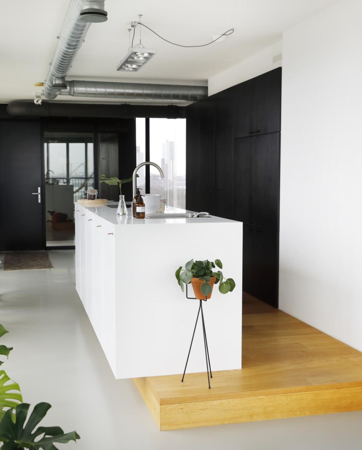 Het witte keukenblok, een ontwerp van Martin, is gemaakt van Corian. De zwarte kast is ook door Martin ontworpen en loopt de hoek om door naar het eetgedeelte. Lamp Rietveld Licht. Witte plantenpot Habitat. Op het aanrecht: glazen vaasje Serax. Bruin flesje waar Leanne een zelfontworpen etiket op heeft geplakt. Witte schaaltjes Ikea. Erachter een weckpot van Cook &amp; Co. Plantenhouder Ferm Living. Rechts grijze kist Loods 5.  vtwonen 05-2018 | fotografie &amp; Styling Peggy Janssen