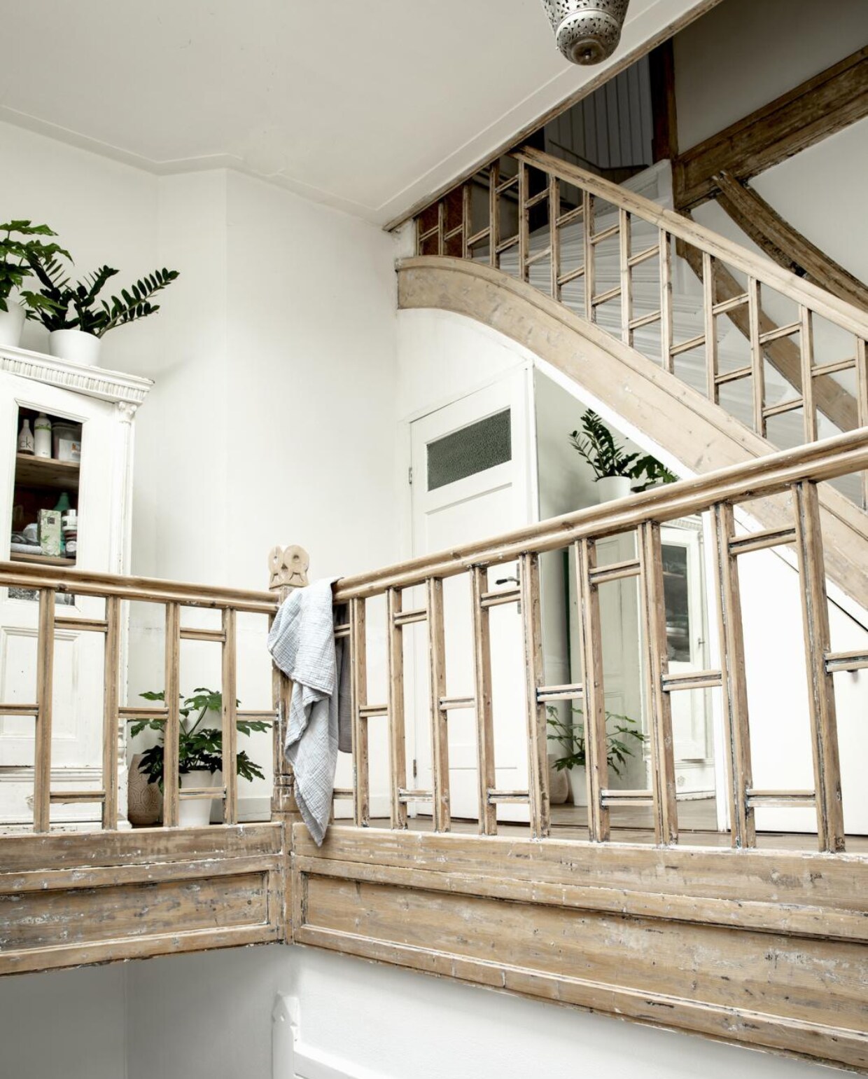 De planten staan in witte potten van Ikea. De spiegel onder de trap zorgt voor een extra ruimtelijk effect. Over de balustrade hangt een grote hydrofieldoek uit de winkel van Dunja. Kast van 2switch, lamp van Meijer+Floor. vtwonen 11-2018 | fotografie Peggy Janssen