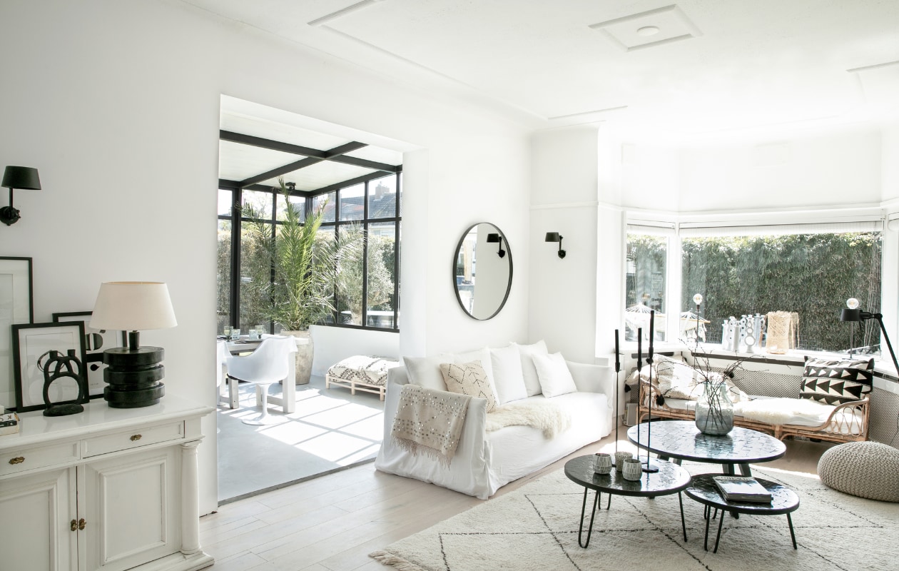 Bank Gervasoni, kaarsenstandaards Loft, plaid uit Marrakech, wandlampen Bolt van Tonone, spiegel Sissy-Boy, salontafels Zenza Home, lamp op buffetkast Casa Gitane, eetkamerstoelen Tulip van Eero Saarinen, eettafel eigen ontwerp, kruikplant Cooperz Wonen, XL poefbank Studio Pure, wandkleur Ral 9010, wit gelakte eikenhouten vloer. Overig onbekend. vtwonen 04-2023 | fotografie Monique Koelman
