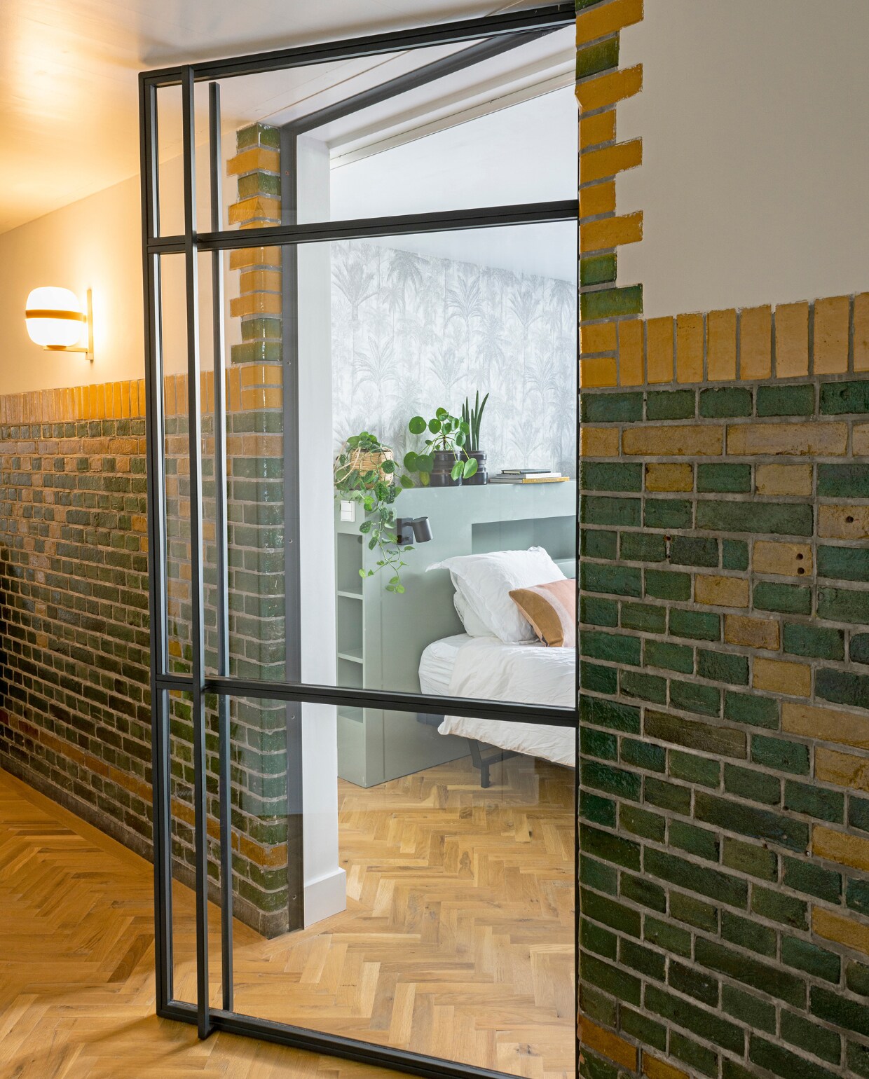 Houten bedombouw gemaakt door de vader van Dorien. Behang Botanical van Dutch Wallcoverings. Zalmroze kussen HKliving. Leeslamp Ikea. vtwonen 12-2020 binnenkijken special | Styling Geertje Planken | Fotografie Caroline Coehorst