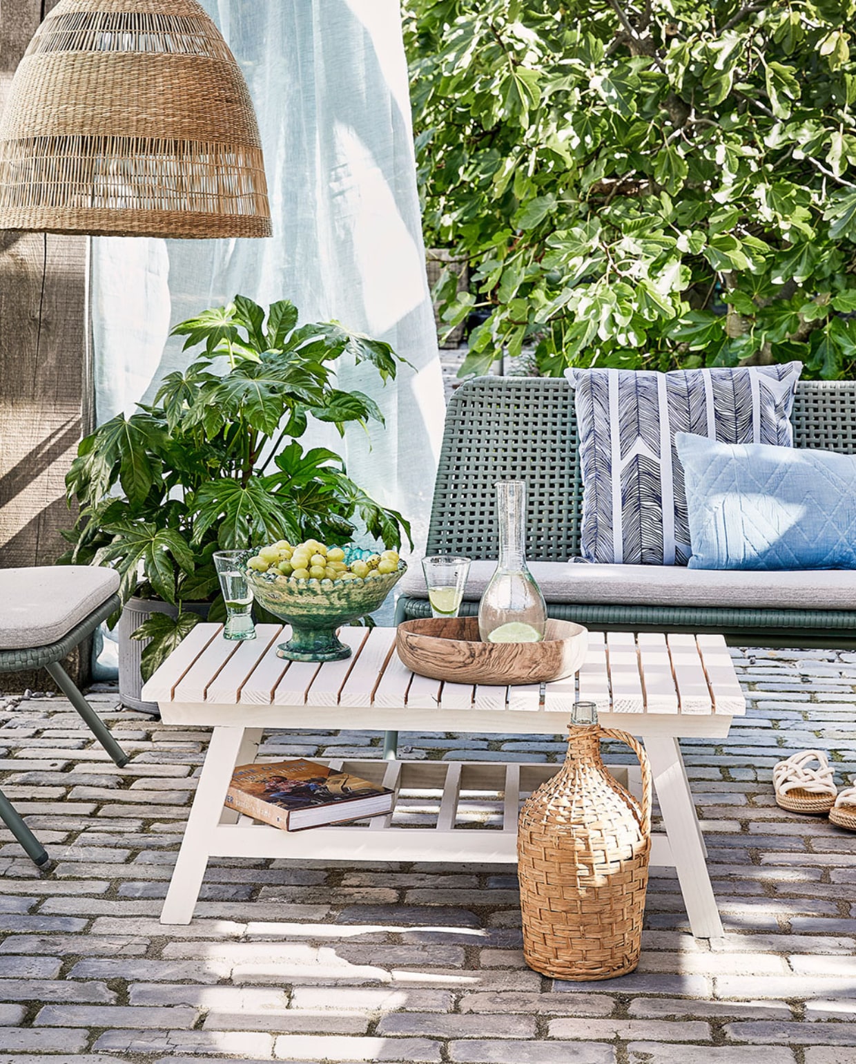 Bank Wivinia € 419,- en stoel Wivinia € 211,50 van Kave Home (vtwonen.nl). Gordijn gemaakt van linnen stof per meter € 25,- (ochreandred.nl). Kussen met print Heringbone € 25,95, lichtblauw kussen Naida € 19,99 (intratuin.nl). Schaal op voet € 99,95, walnoothouten schaal € 75,-, glazen karaf Cigogne € 23,50, glazen op voet Diabolo per stuk € 6,80 (householdhardware.nl). Instappers € 35,99 (zarahome.com). Rieten lamp Torared € 39,95 (ikea.com). Plaid Native Fan € 34,99 (sissy-boy.com). Sisal kussen € 25,- (loods5.nl). Overig privébezit. vtwonen tuin special 04-2021 | productie Corrien Flohil | uitvoering Johan Snoodijk @snoodijkenco | styling Moniek Visser | fotografie Peggy Janssen