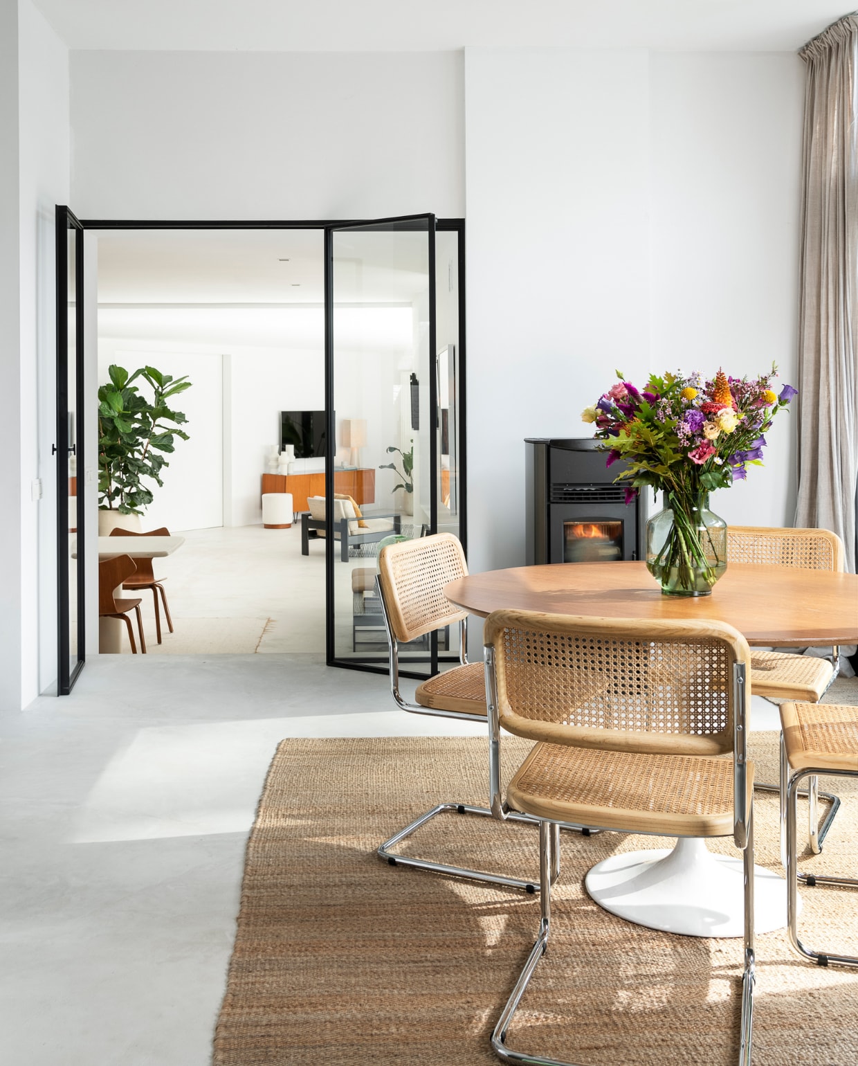 Vloer Terra Logica van Terra International. Stoelen Swing en vloerkleed Killia van Furnified. Vintage tafel Brussels Design Market. Vaas HKliving. Pelletkachel Superior Stufe. Deuren op maat gemaakt Philip V. Achter de deuren eettafel Pim en dressoir Pisa van Furnified, vazen House Doctor, tafellamp HKliving, fauteuil vintage. vtwonen 05-2023 | fotografie Jonah Samyn