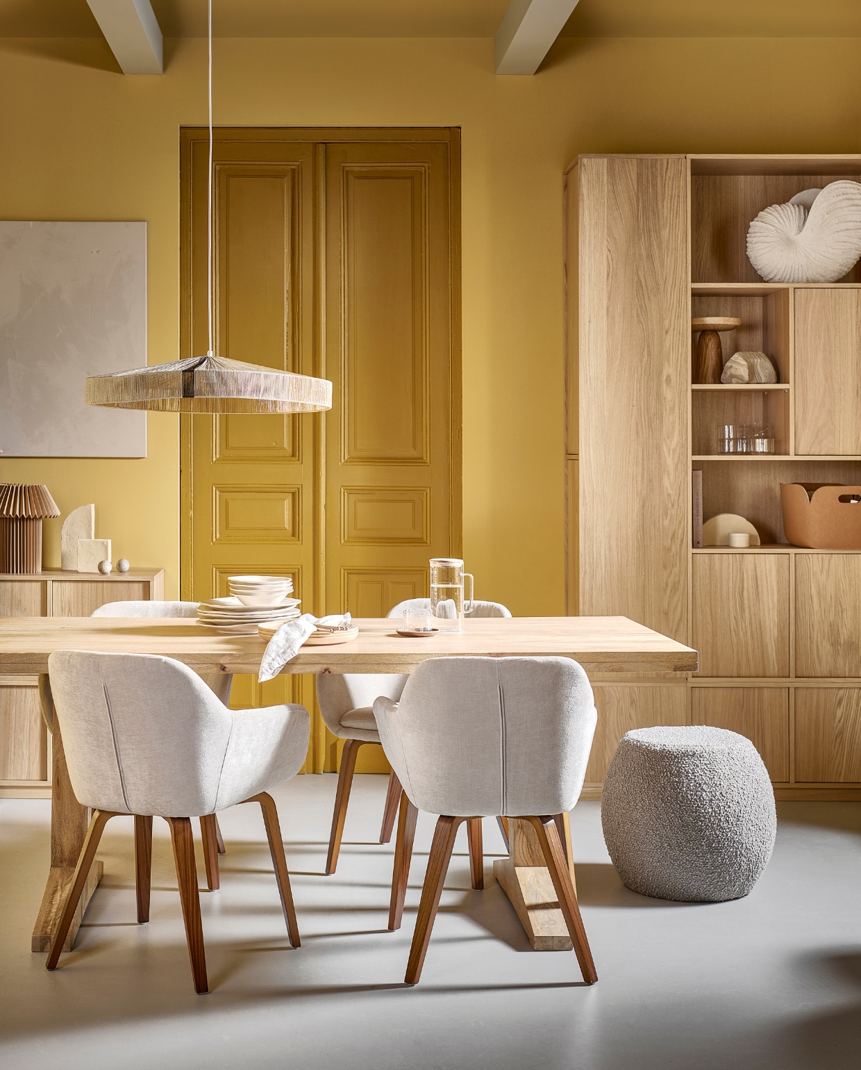 Eetkamerstoelen Base met fluwelen zitting in zand, 58x58x80 cm (bxdxh) € 199,-. Mangohouten eettafel Deck in Naturel, 200x90x78 cm (lxbxh) € 899,-, ook in 120 cm (Ø) in Clay € 749,-. Bouclé poef Soft Bubble in lichtgrijs, 46x45 cm (Øxh) € 119,-, ook in stervorm Soft Star.  Eikenhoutfineer onderkast Modulair, 40x40x44 cm (bxdxh) € 169,-, de Modulair onderkasten zijn verkrijgbaar in breedtes: 40 cm, 77 cm en 110 cm. M.m.v. vtwonen.nl/shop (schelpornament van Nordal, opbergmand van Muuto, stenen sculpturen van Ferm Living, muurverf in Straw, lakverf deur in Desert), hm.com (papieren tafellamp), sissy-boy.com (gele aardewerken borden, houten etagère), zarahome.com (aardewerken borden, bestek, linnen servet, glazen karaf met deksel, waterglas, notenhouten onderzetter), flinders.nl (hanglamp Rope van HKliving). Overig privébezit. vtwonen 05-2023 | productie Tanja Taarberg | styling Sanne Ketelaar | fotografie Sjoerd Eickmans