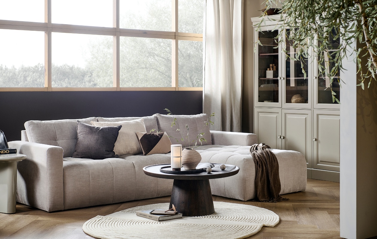 Bank Bar met chaise longue rechts in zand, 280x170x87 cm (bxdxh) € 1749,-, ook met chaise longue aan de linkerkant en in antraciet, groen, roze en warmgrijs. Grenenhouten vitrinekast Chow 2-deurs in Dakargrau, 54x40x215 cm (bxdxh) € 499,-, ook verkrijgbaar als 4-deurs vitrinekast. Walnotenfineer salontafel Coffee a Gogo, 90x40 cm (Øxh) € 499,-. Mangohouten bijzettafel Beach Small in Clay, 64x51x53 cm (lxbxh) € 319,-, ook in 80x80x41 cm (lxbxh).M.m.v. vtwonen.nl/shop (vloerkleed van Bolia, tafellamp van Menu, gestreept kussen van Moos), hm.com (beige aardewerken vaas, bruine plaid), karwei.nl (muurverf Mirre en Warm Brown). Overig privébezit. vtwonen 05-2023 | productie Tanja Taarberg | styling Sanne Ketelaar | fotografie Sjoerd Eickmans