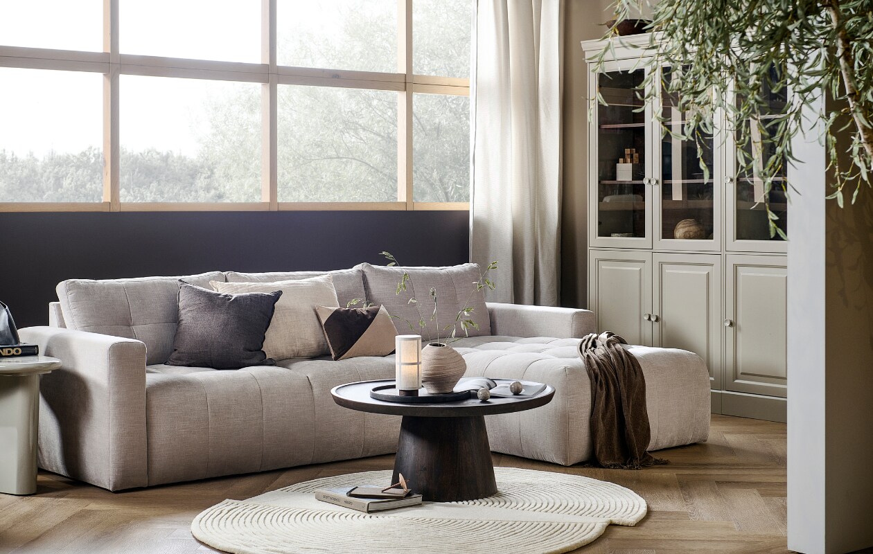 Bank Bar met chaise longue rechts in zand, 280x170x87 cm (bxdxh) € 1749,-, ook met chaise longue aan de linkerkant en in antraciet, groen, roze en warmgrijs. Grenenhouten vitrinekast Chow 2-deurs in Dakargrau, 54x40x215 cm (bxdxh) € 499,-, ook verkrijgbaar als 4-deurs vitrinekast. Walnotenfineer salontafel Coffee a Gogo, 90x40 cm (Øxh) € 499,-. Mangohouten bijzettafel Beach Small in Clay, 64x51x53 cm (lxbxh) € 319,-, ook in 80x80x41 cm (lxbxh).M.m.v. vtwonen.nl/shop (vloerkleed van Bolia, tafellamp van Menu, gestreept kussen van Moos), hm.com (beige aardewerken vaas, bruine plaid), karwei.nl (muurverf Mirre en Warm Brown). Overig privébezit. vtwonen 05-2023 | productie Tanja Taarberg | styling Sanne Ketelaar | fotografie Sjoerd Eickmans