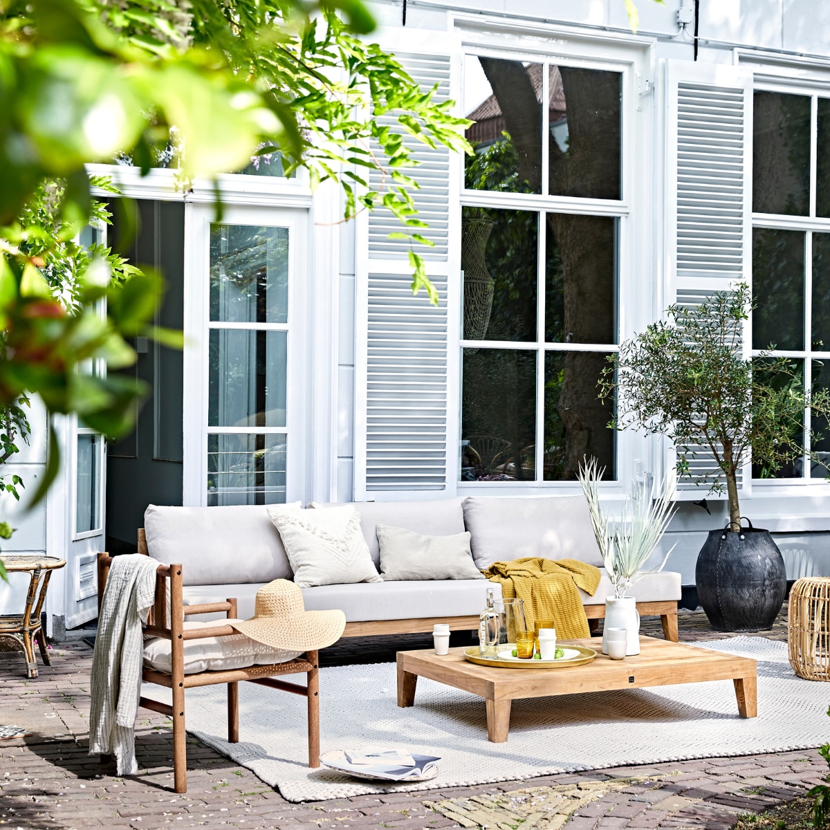 Buitentafel MBrace van Dedon 200x90 cm, houten stoelen Tibbo van Dedon (dacks.nl). Witte bistro klapstoelen van Fermob, witte armstoel Luxembourg van Fermob, Serviesgoed uit 12-delige dinner box Nordic Sand van Broste Copenhagen, schaal Nordic Sand van Broste Copenhagen ø 22,5 cm, Serax Surface longdrinkglas Serax Surface 4 stuks, linnen tafelkleed Gracie van Broste Copenhagen 160x300 cm (vtwonen.nl). Gele servetten en wit linnen plaid (nordal.eu). Keramieken schaal op klapstoel, linnen lampionnen (sukha.nl). Ladder vanaf (com-anders.nl). Witte vaas (zarahome.com). Stonewashed bestekset Brick Lane 39-delig (luxerybynature.nl). Glazen kan (weldaad.com). Klapkruk van mangohout (hm.com). Okergeel kussen (madamstoltz.dk). vtwonen 07-2020 | styling Cleo Scheulderman | fotografie Jeroen van der Spek
