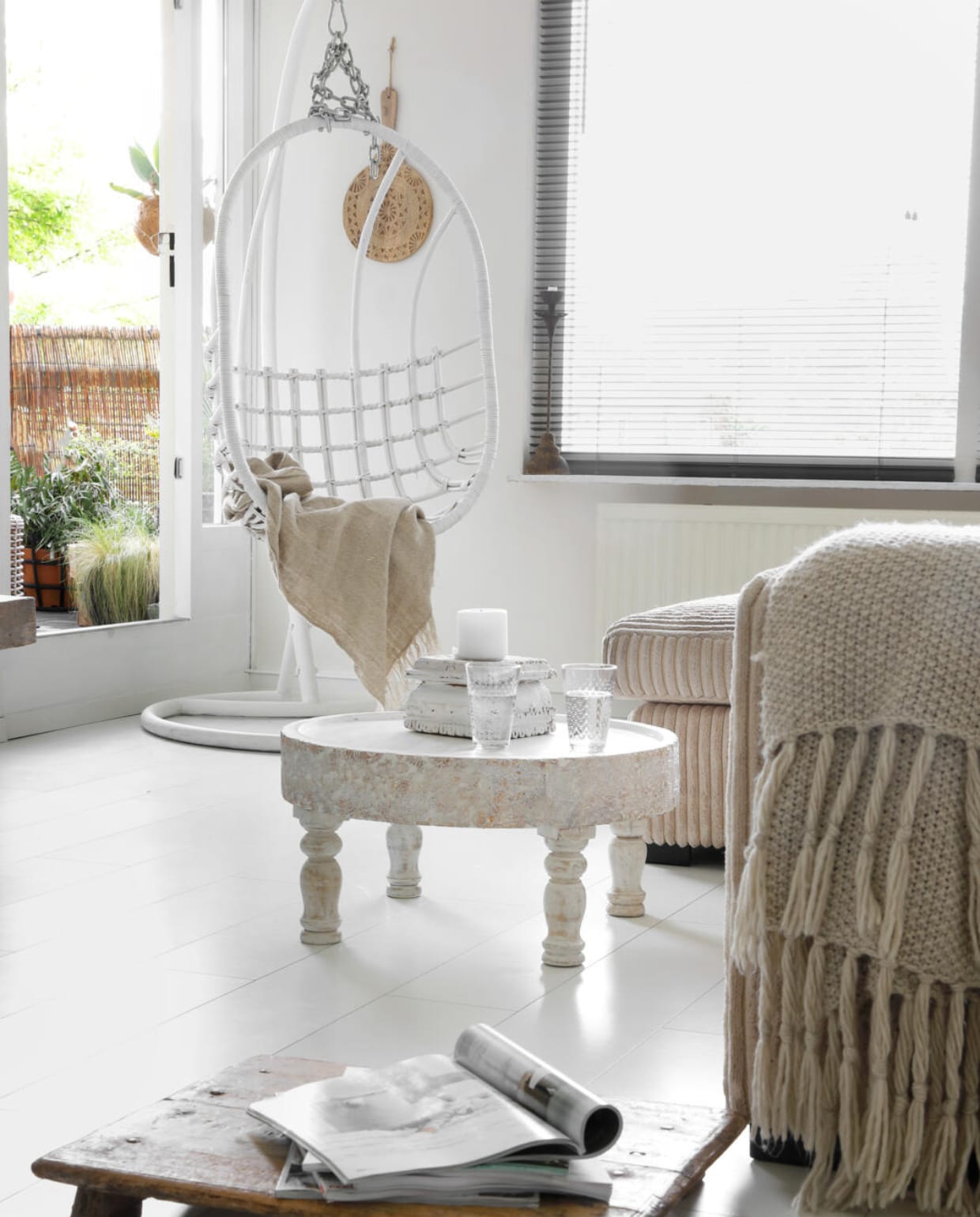 Voor de deur naar het balkon staat een witte hangstoel van Sissy-Boy. Erin een kussen van H&amp;M Home en nummer8stoerwonen. Plaid Kwantum. Aan de muur een gedecoreerde houten snijplank van Zenza. vtwonen 03-2018 | fotografie Peggy Janssen