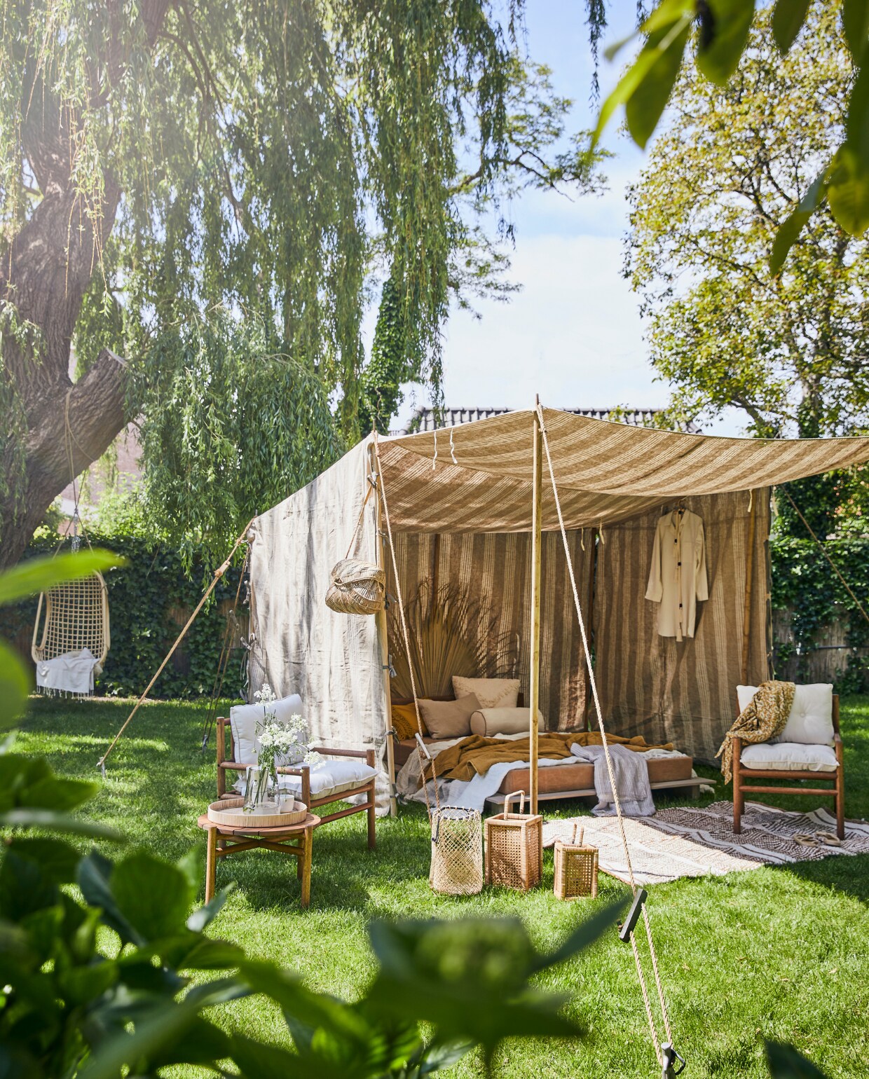 Tent op maat gemaakt, prijs op aanvraag, bed met canvas matras vanaf € 700,-(com-anders.nl). Marantiehouten fauteuil met witte kussens € 149,-, bijzettafel 38x50 cm (hx Ø) € 99,-, lichtbeige vloerkleed, 140x200 cm € 179,- (hm.com). Palmblad € 22,-, wit kussen met franjes 50x50 cm € 55,25, okergeel kussen € 28,-, wit linnen rolkussen € 39,25, gele gedessineerde kimono € 56,50 (madamstoltz.dk). Rotan dienblad € 49,-, glazen kan € 33,50 (weldaad.com). Zandkleurig linnen kussen € 34,95, okergele quilt € 72,- (iblaursen.nl). Rotan hangstoel van HKliving € 199,95, windlicht Ewald van Nordal, groot € 79,95, klein € 59,95 (vtwonen.nl). Wit linnen plaid € 304,75, gestreept katoenen plaid € 59,- (nordal.eu). Mok op dienblad € 16,-, rieten tas € 129,-, keramieken kan € 99,- (sukha.nl). Pyjama € 45,99, slippers € 29,99 (zarahome.com). vtwonen 07-2020 | styling Cleo Scheulderman | fotografie Jeroen van der Spek