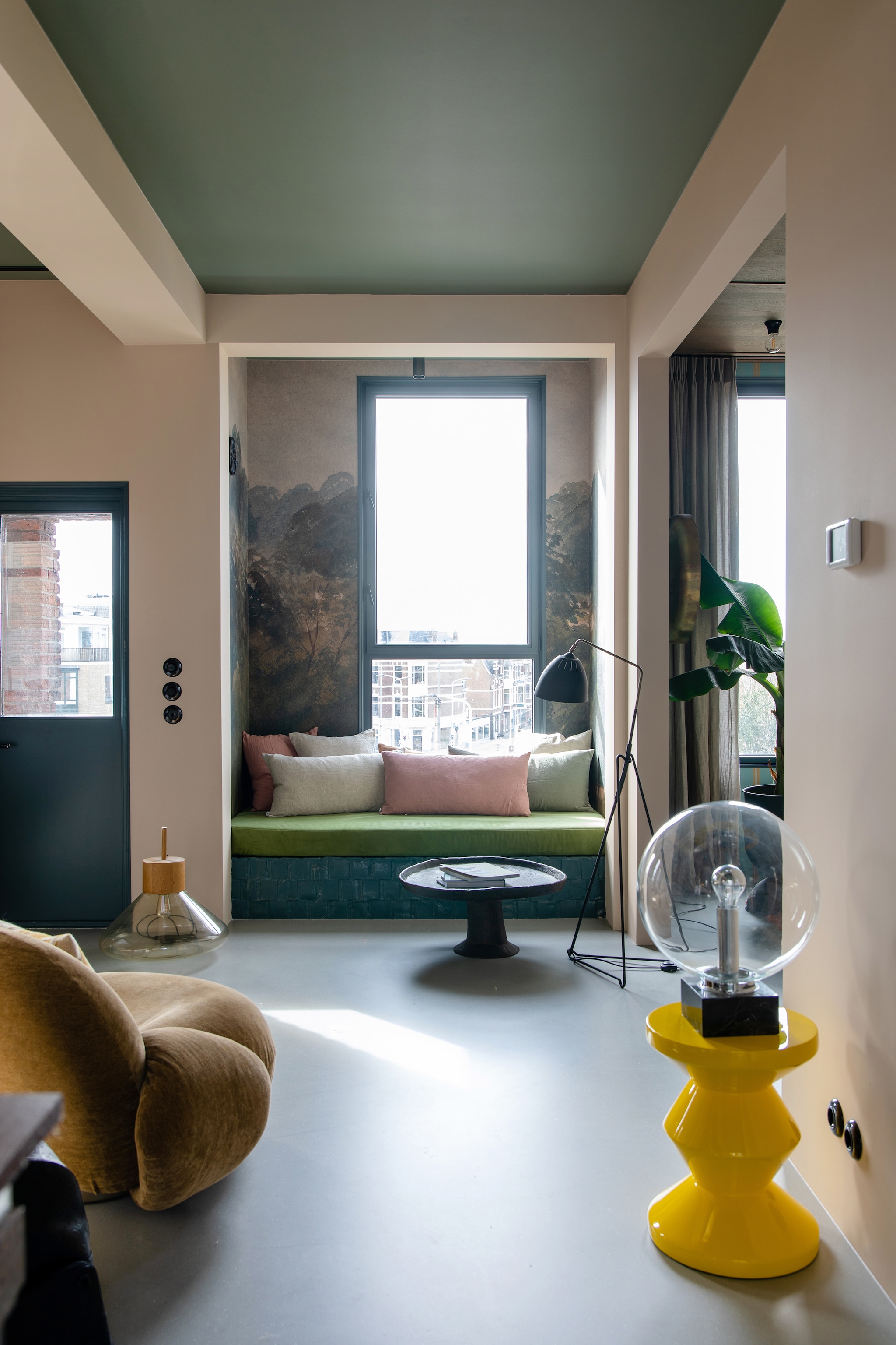 Glazen vloerlamp Brokis, bakelieten stopcontacten en schakelaars De Oude Schakelaar. Behang Selected Wallpaper, plafondlamp Serax. Linnen kussens By Mölle, tegels daybed Daniel van Dijck. Antieke zwarte bijzettafel gekocht in de Antwerpse Kloosterstraat, tafellamp op bijzettafel vintage, gele bijzettafel Polspotten, fauteuil Pacha van Gubi via Loft76. Muurverf plafond Soothing Moss, muurverf muren Subtle Umber, lakverf deur Puur Marmer van Flexa. Gietvloer Senso. vtwonen 05-2023 | styling &amp; fotografie Theo-Bert Pot &amp; Jelle van de Schoor