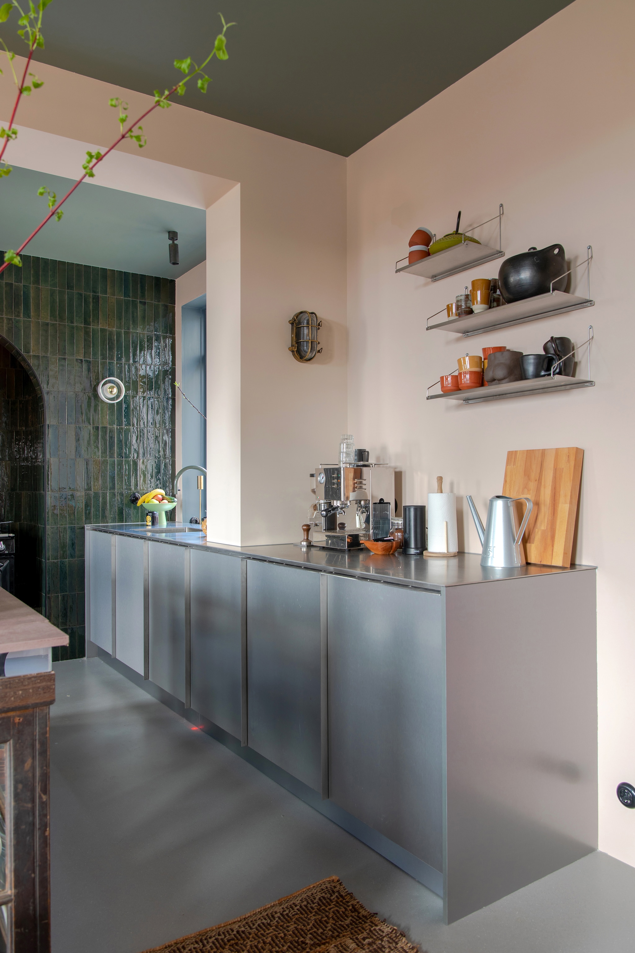 Rvs keuken Houtmerk. Muurverf plafond Soothing Moss en muurverf muren Subtle Umber van Flexa. Wandtegels Olivia van Sanitairwinkel, gietvloer Senso, kraan Quooker gespoten in kleur Ral 6011 door Koperenkranen. Ronde wandlamp Tom Dixon, zwarte wandlamp bouwmarkt. Koffiemachine vintage, koffiekan Piet Hein Eek, snijplank Dok, wandplanken Frama, mokken Edwin Pelser en Merci Paris, theepot Serax. vtwonen 05-2023 | styling &amp; fotografie Theo-Bert Pot &amp; Jelle van de Schoor