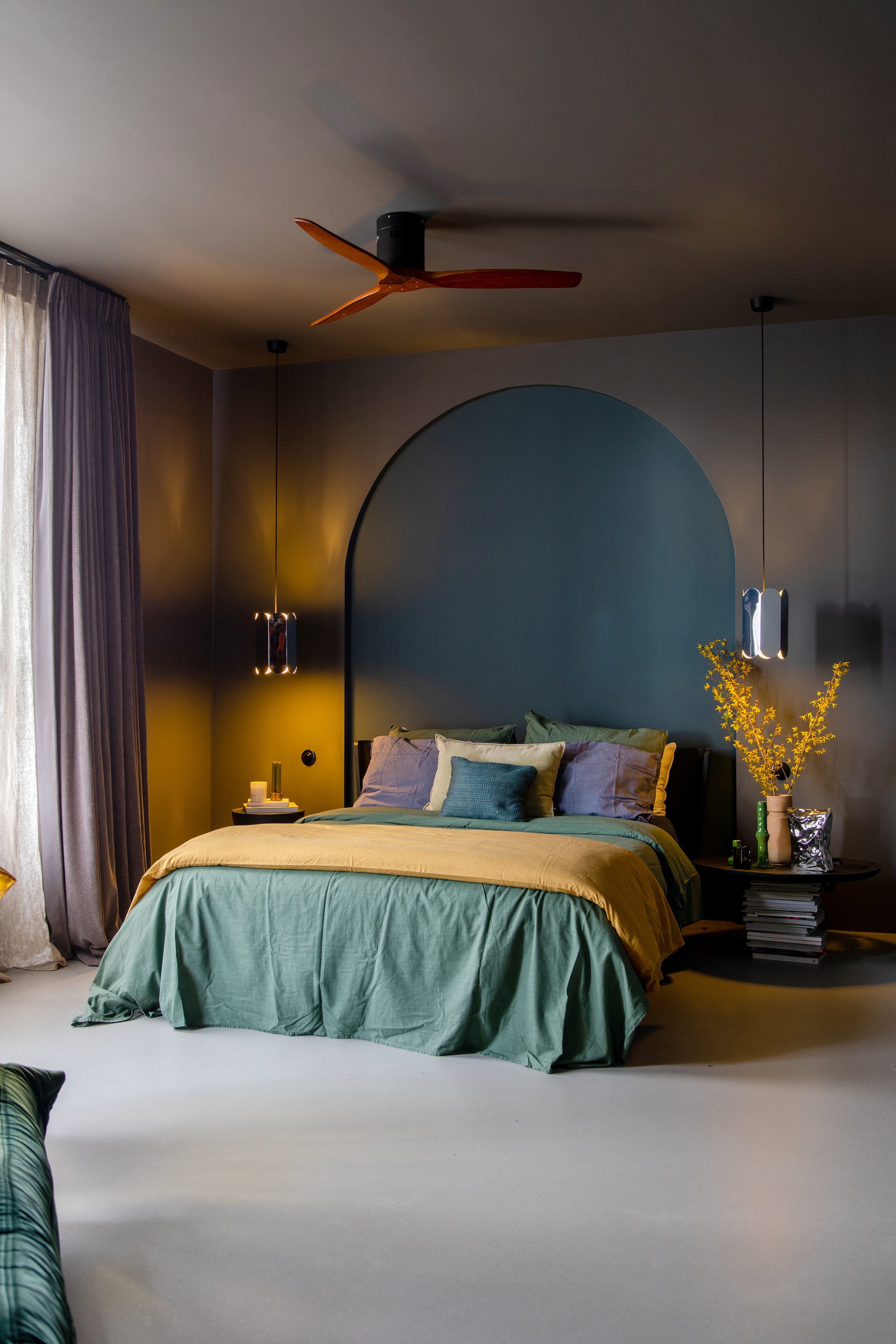 Gietvloer Senso, verf muren en plafond 85% Grafiet, muurverf nis Puur Marmer van Flexa. Ventilator Bol. Linnen gordijnen Holland Haag, hanglampen Hay. Hoofdkussens en beddengoed Walra, bed Auping. Groene kandelaar en chipszak-vaas HKliving, aardewerken vaas MaisonNL, nachtkastje zelfgemaakt van een stapel tijdschriften en een houten dienblad. vtwonen 05-2023 | styling &amp; fotografie Theo-Bert Pot &amp; Jelle van de Schoor