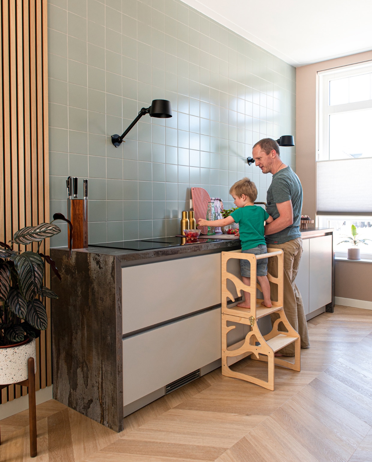 Eikenhouten wandpaneel WoodUpp, plantenstandaard Made. Keuken SieMatic in Sterling Grey, omkasting Dekton Trilium van Cosentino, lampen Tonone, tegels Global Collection van Mosa Tiles. Magnetisch messenblok Rokkakkei, houten trap Learning Tower via Etsy, zout- en pepermolen Menu, snijplank Wye Design, dienblad Prchtg, viskaraf Fonq. Muurverf Dead Salmon van Farrow &amp; Ball, pvc-vloer in Hongaarse punt Chevron 6541 van Therdex. Overig onbekend. vtwonen 05-2023 | productie De Binnenkijkers | styling Jeske Weel | fotografie Caroline Coehorst