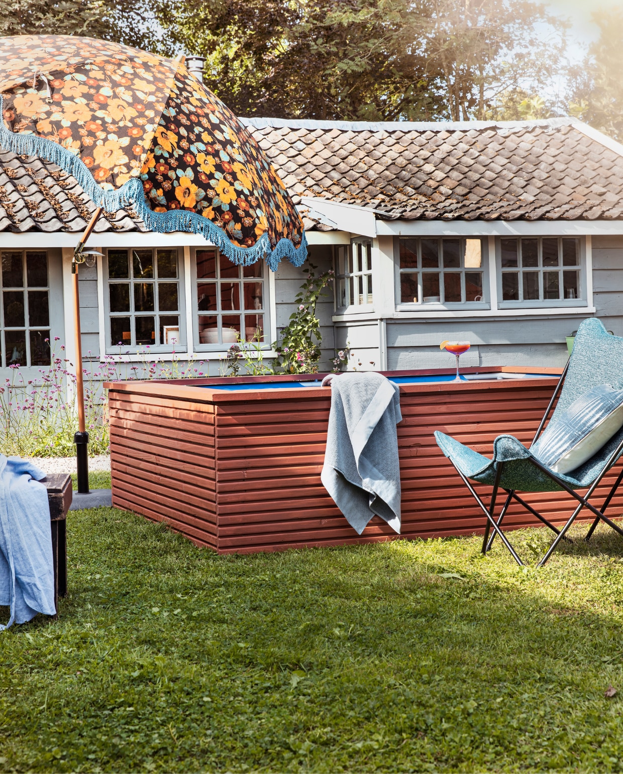 Zwembadombouw geschilderd met Traditional Paint Dry Terra, per liter € 59,40 (pure-original.nl). Loungestoel Sphinx van Lafuma in Cobalt, staal en Sunbrella-stof € 284,99, parasol Floral Energy van HKliving € 369,- (vtwonen.nl)/shop). Badlaken Basic € 14,99 (hm.com). Blauwe overhemdjurk € 39,99 (zara.com). Kussen tie-dye € 19,95 (loods5.nl). Overig privébezit. vtwonen tuin special 08 | productie Corrien Flohil | styling Moniek Visser | uitvoering zwembadombouw Studio Milo