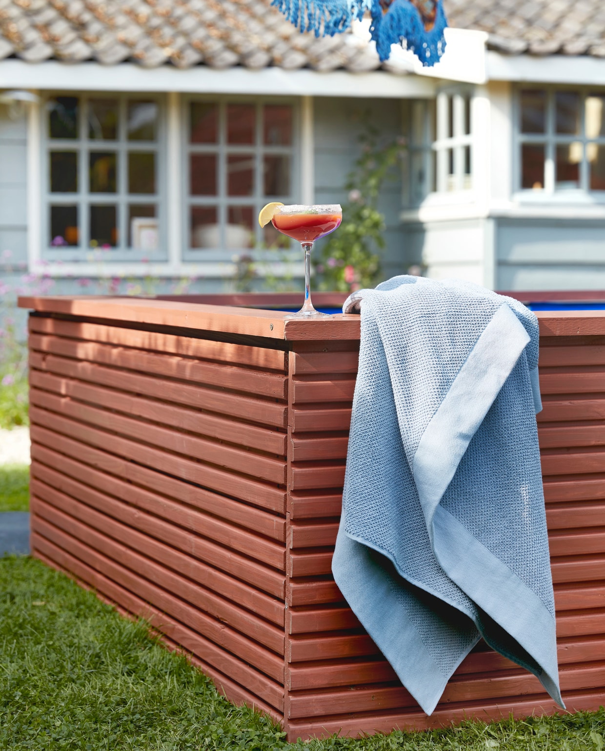 Zwembadombouw geschilderd met Traditional Paint Dry Terra, per liter € 59,40 (pure-original.nl). Parasol Floral Energy van HKliving € 369,- (vtwonen.nl)/shop). Badlaken Basic € 14,99 (hm.com). Overig privébezit.