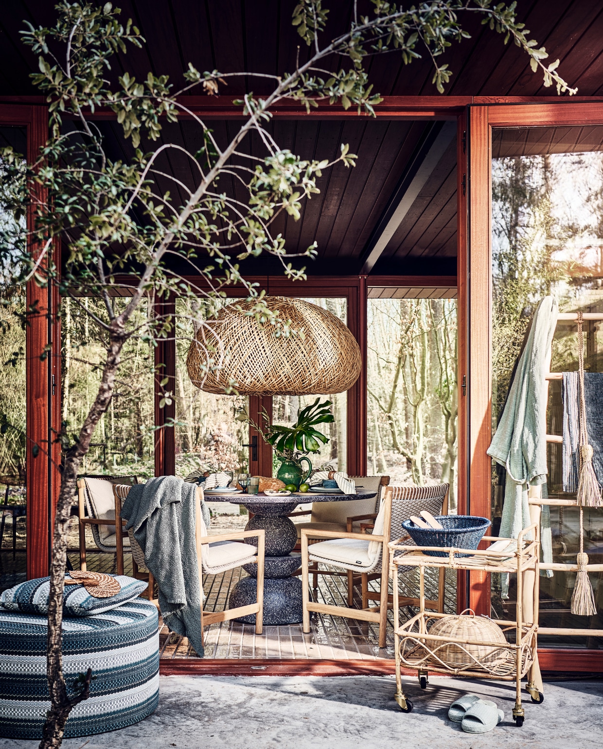 Tafel voor binnen en buiten, 130 cm (Ø) vanaf € 2495,- (lanena-home.com). Duurzaam teakhouten stoelen, per stuk € 1675,-, poef met print € 949,-, kussen met print € 169,- (dacks.nl). Badjas € 285,-, blauwe plaid € 325,- (brechtmurreatelier.nl).  Rotan lamp Nido, 115x110x62 cm (lxbxh) € 1590,-, waaier € 36,-, bamboe trolley, 55x44x80 cm (lxbxh) € 275,-, olijfhouten ladder € 285,-, palmblad schaal op trolley uit Burkina Faso € 19,-, blauw gerecycled waterglas Bubbel € 11,-, blauw gerecycled wijnglas € 15,-, langwerpig bord van Wonki Ware € 14,-, slinger van gras € 33,-, hanglamp € 343,- (couleurlocale.eu). Kan € 59,-, gestreepte theedoek aan ladder € 8,95, bakjes in vorm van vis op trolley € 17,95 (maisonnl.com). Bestek, 16-delig € 89,99, afdekmand in trolley, prijs op aanvraag, servetring, set van 2 € 7,99, placemat, set van 2 € 4,99 (hm.com). Slabestek € 19,95 (urbannatureculture.com). Slippers € 25,99, servet € 6,99 (zarahome.com). Blauw servies Matera van Leonardo, 18-delig € 140,99 (vtwonen.nl/shop). Takken, prijs op aanvraag (plantje.nl). vtwonen 06-2023 | styling Liza Wassenaar | fotografie Sjoerd Eickmans