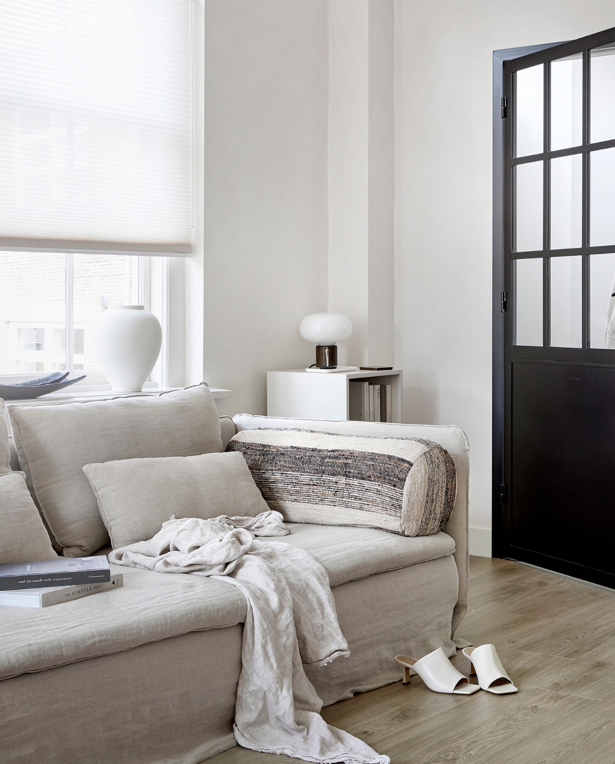 EVC vloer Oat, per m² € 39,99. M.m.v. karwei.nl (op maat gemaakt lichtdoorlatend plisségordijn in kleur Linnenbeige A 18074), ikea.nl (bank Söderhamn), bemz.com (linnen bankhoes), zarahome.com (linnen plaid, zwarte schalen, witte vaas), stories.com (schoenen), casagitane.com (rond kussen Tronc), newworks.dk (tafellamp), bauwerkcolour.com (muurverf in kleur Mykonos). Overig privébezit. vtwonen 08-2021 | productie Tanja Saarberg | styling Kim van Rossenberg | fotografie Peggy Janssen