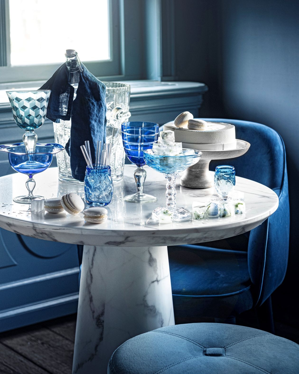 Poef van Minotti € 1150,-(covanderhorst.nl). Stoel Cosy van PolsPotten € 302,99 (vtwonen.nl). Wijnkoeler€ 175,- (pietjonker.nl). Blauw wijnglasmet print links, set van 6 € 129,-, blauwgestreept wijnglas in het midden, set van 6€ 129,- (polspotten.nl). Waterkaraf metdop, prijs op aanvraag (sostrenegrene.com).Blauw glas linksonder € 10,- (loods5.nl).Glazen rietjes, set van zes € 10,50(bijenkorf.nl). Taart gemaakt naar wens€ 32,95 (huizevanwely.nl). Gebobbeldglas € 30,-, gebobbelde ijscoupe metijsklontjes € 50,-, smal gebobbeld blauwglas € 20,-, linnen servet, set van 2 € 9,99(hm.com). Zelfgemaakte ijsklontjesmet blaadjes en bloemetjes erin. Overigprivébezit. vtwonen 07-2020 België | fotografie Sjoerd Eickmans | styling Liza Wassenaar