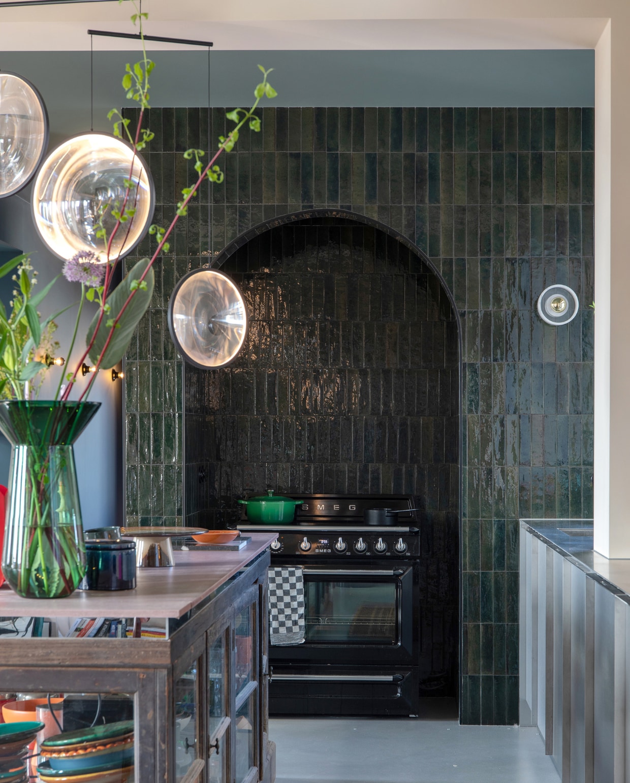 Wandtegels Olivia via Sanitairwinkel, fornuis Smeg, groene pan Le Creuset, zwarte steelpan Serax, theedoek Dok, aardewerken pot en vitrine vintage, hanglamp Dcw Editions, groene vaas Polspotten. vtwonen 05-2023 | styling en fotografie Theo-Bert Pot, Jelle van de Schoor
