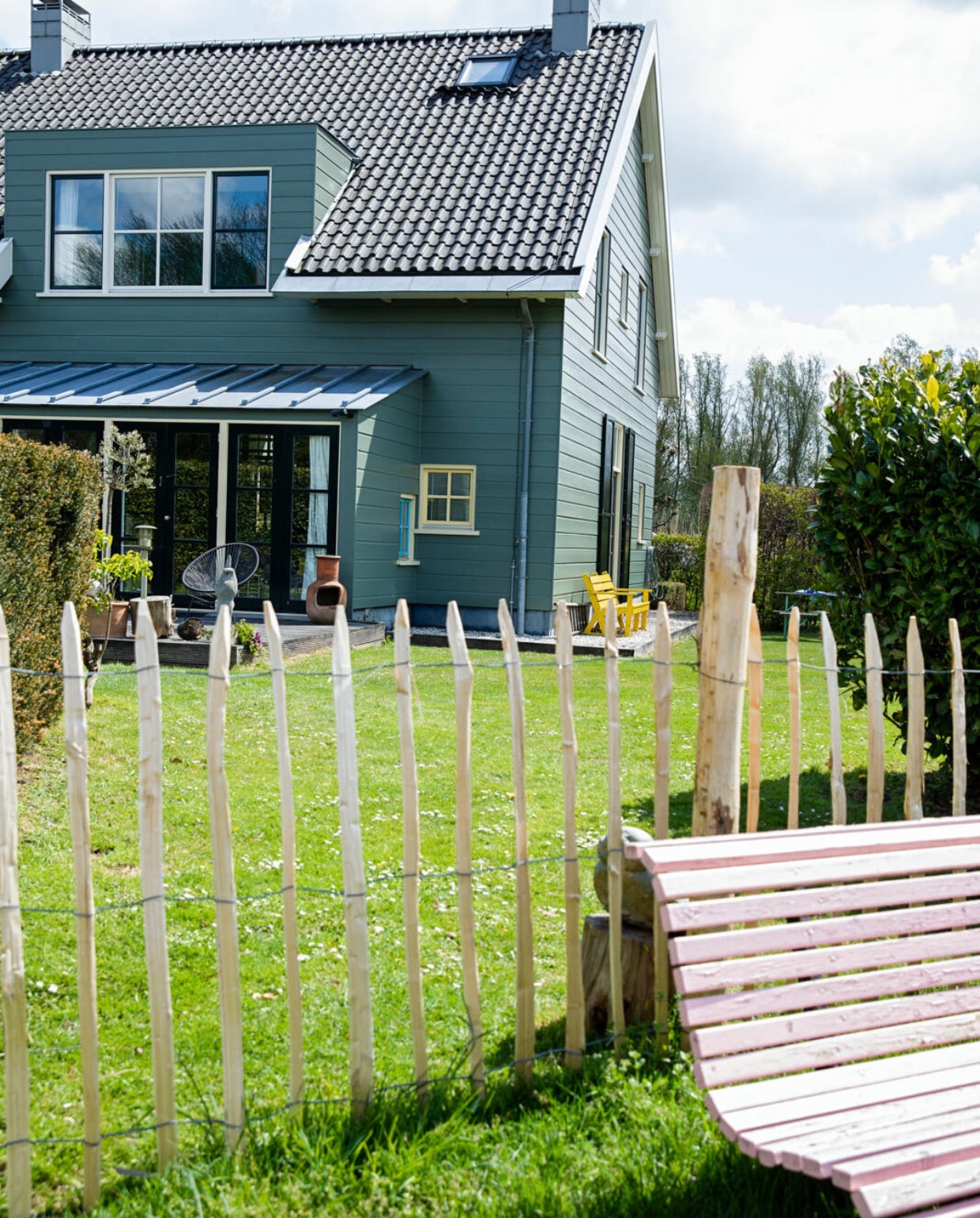 Het huis is aan de buitenkant afgetimmerd met hout, maar heeft een betonnen constructie. De kleur is bepaald door de monumentencommissie en mag niet worden veranderd. Tuinbankje geschilderd in Nancy’s Blushes van Farrow &amp; Ball. vtwonen 07-2021 | styling Ilona Jongepier | fotografie Dana van Leeuwen